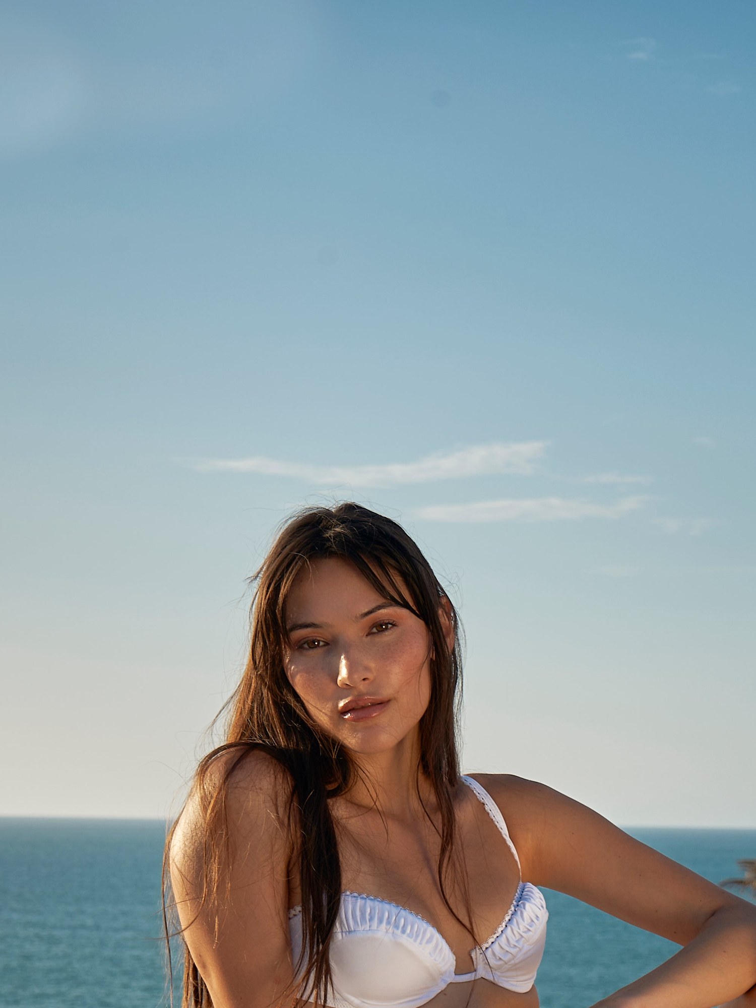 Model in a white bikini top seated on a white dome by the sea