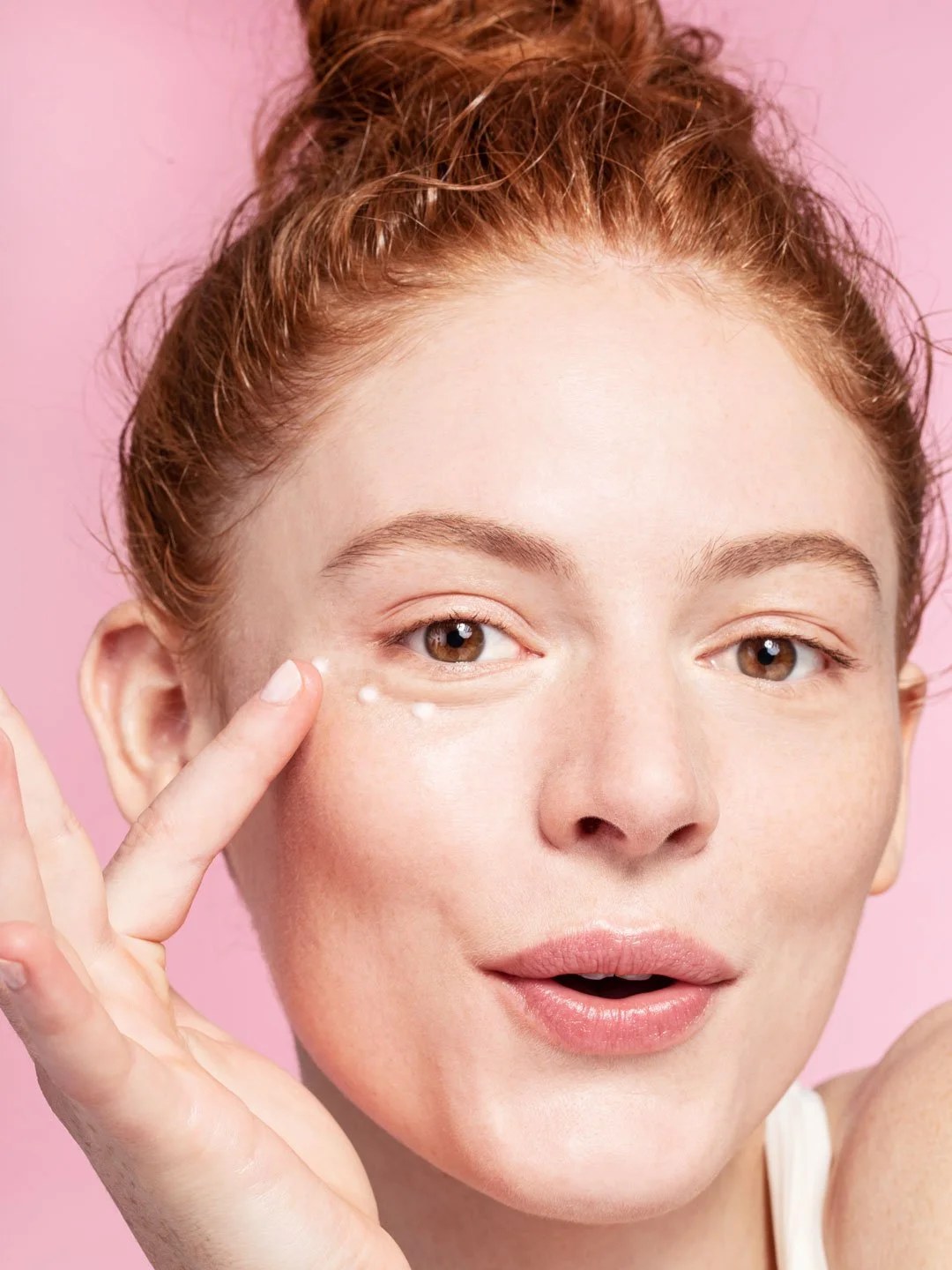 Model applying Saturday Skin eye cream against a pink studio backdrop