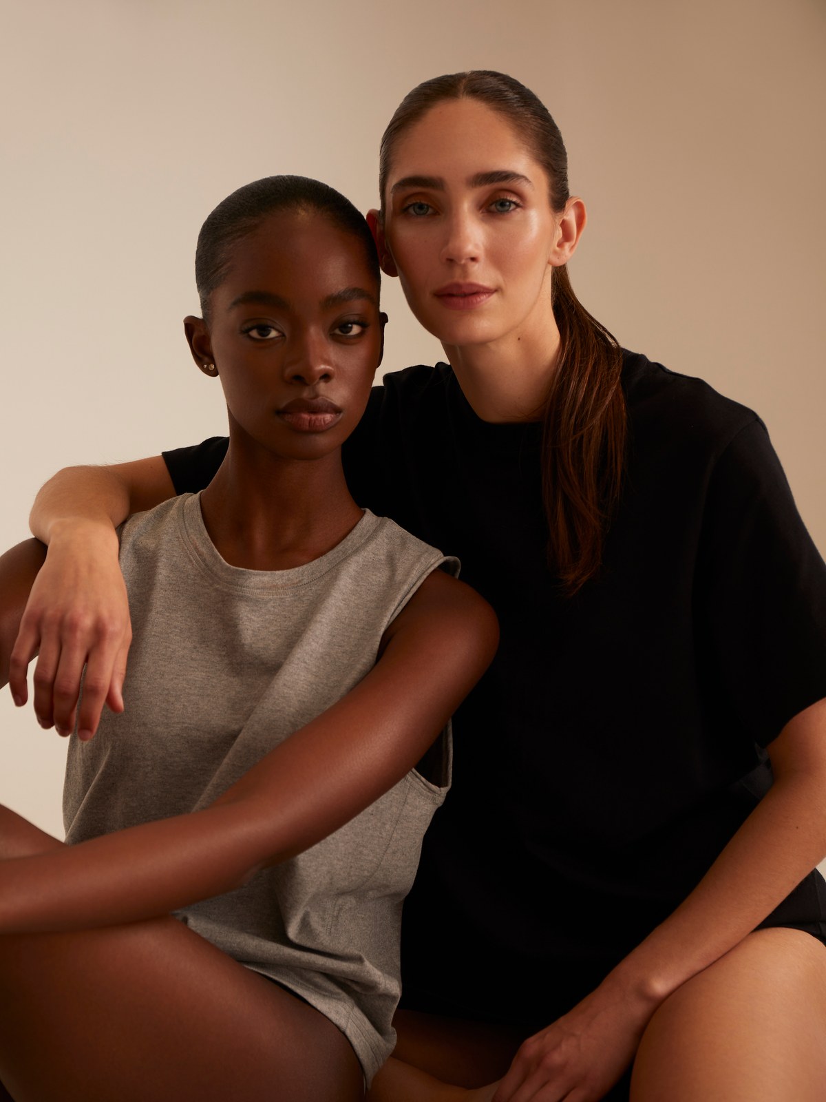 Two women in neutral TKEES basics seated together in a studio