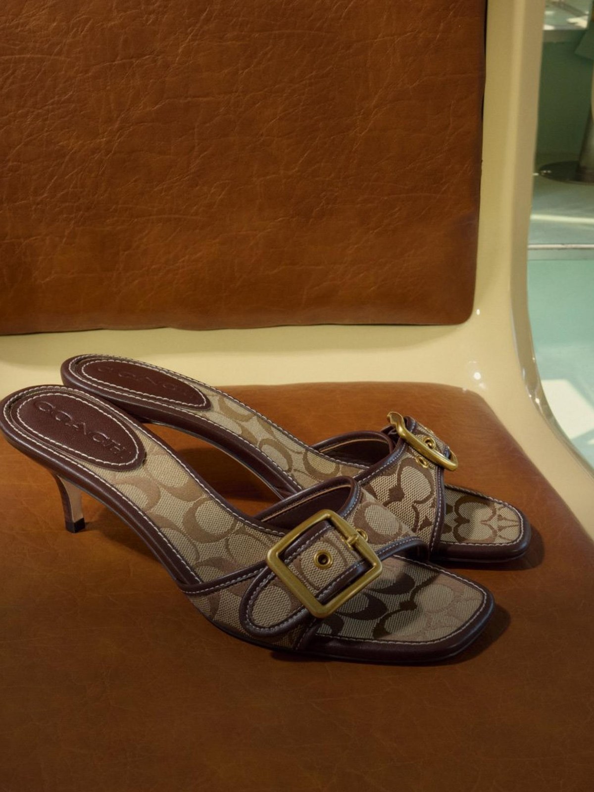 Monogram canvas kitten heel slide sandals on a tan leather seat