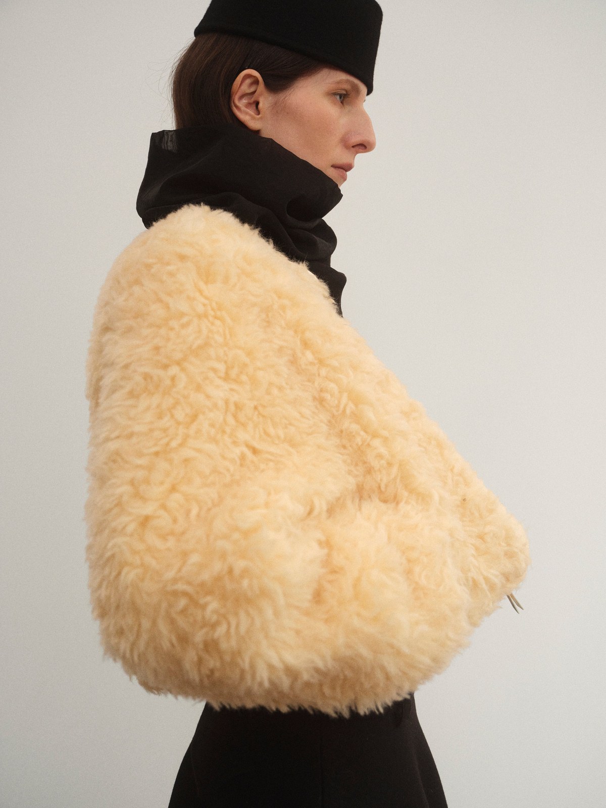 Model in a cream shearling jacket and black head wrap against a pale studio backdrop