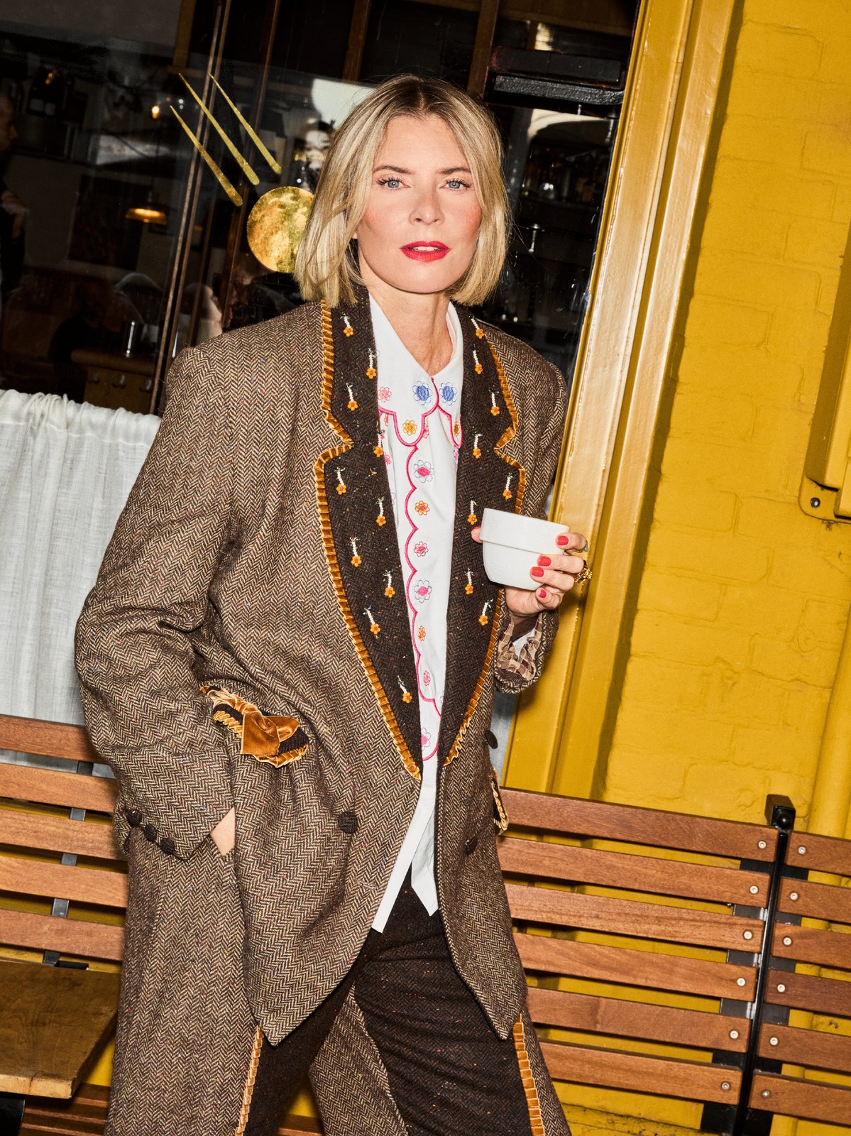 Woman in a textured brown jacket over a white floral shirt on a bench