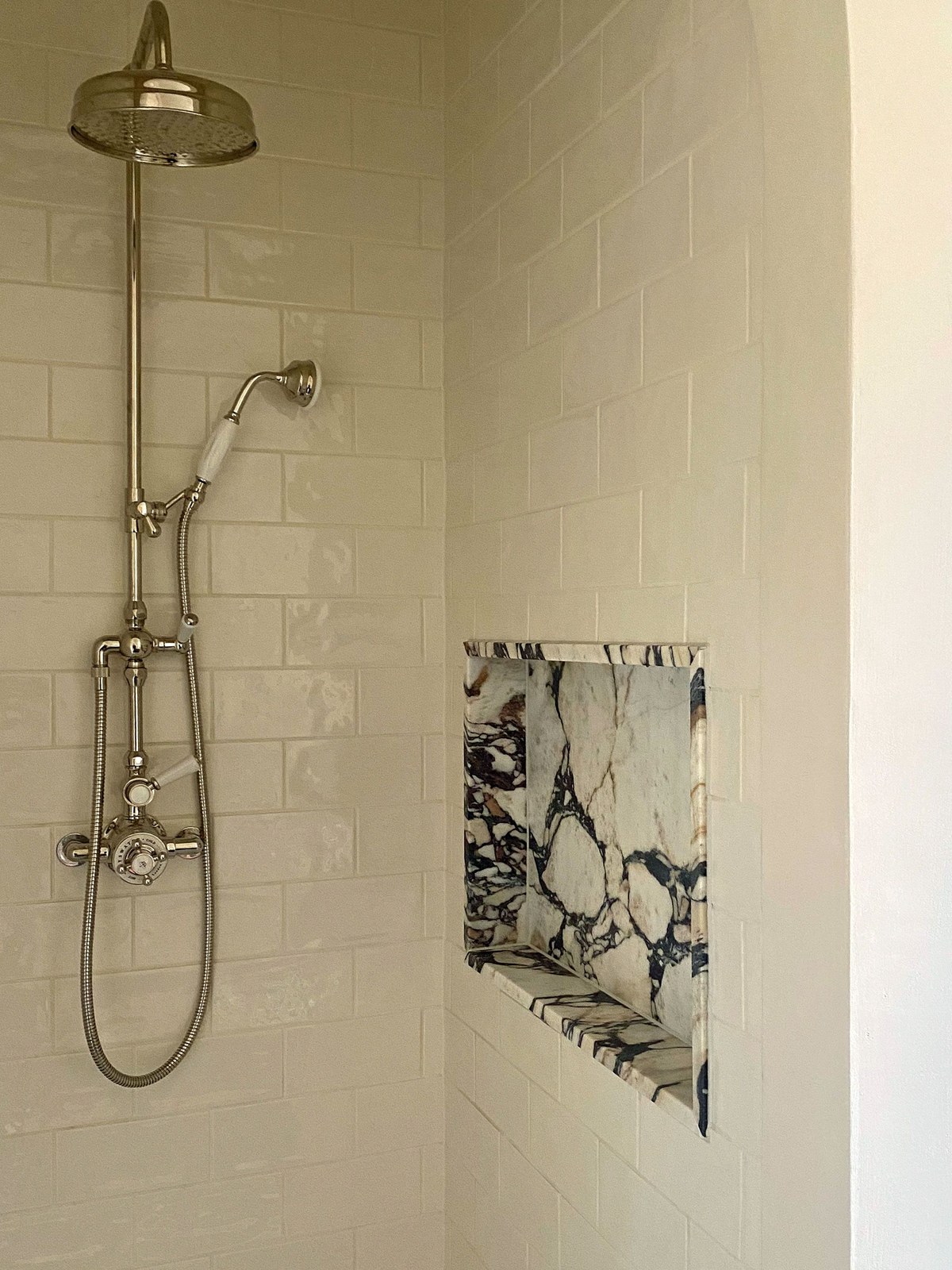 Cream tiled shower with an exposed brass shower system and a niche