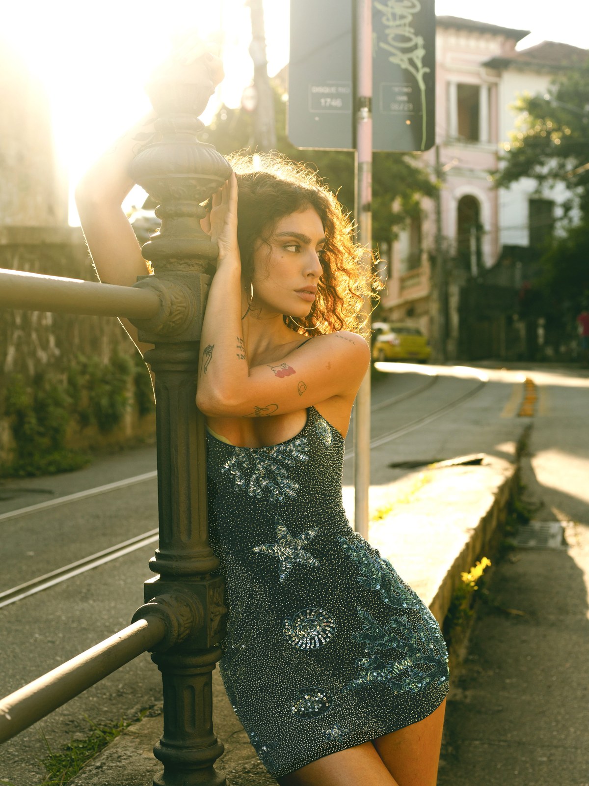 Woman in a dark embellished mini dress leaning beside a city streetlamp