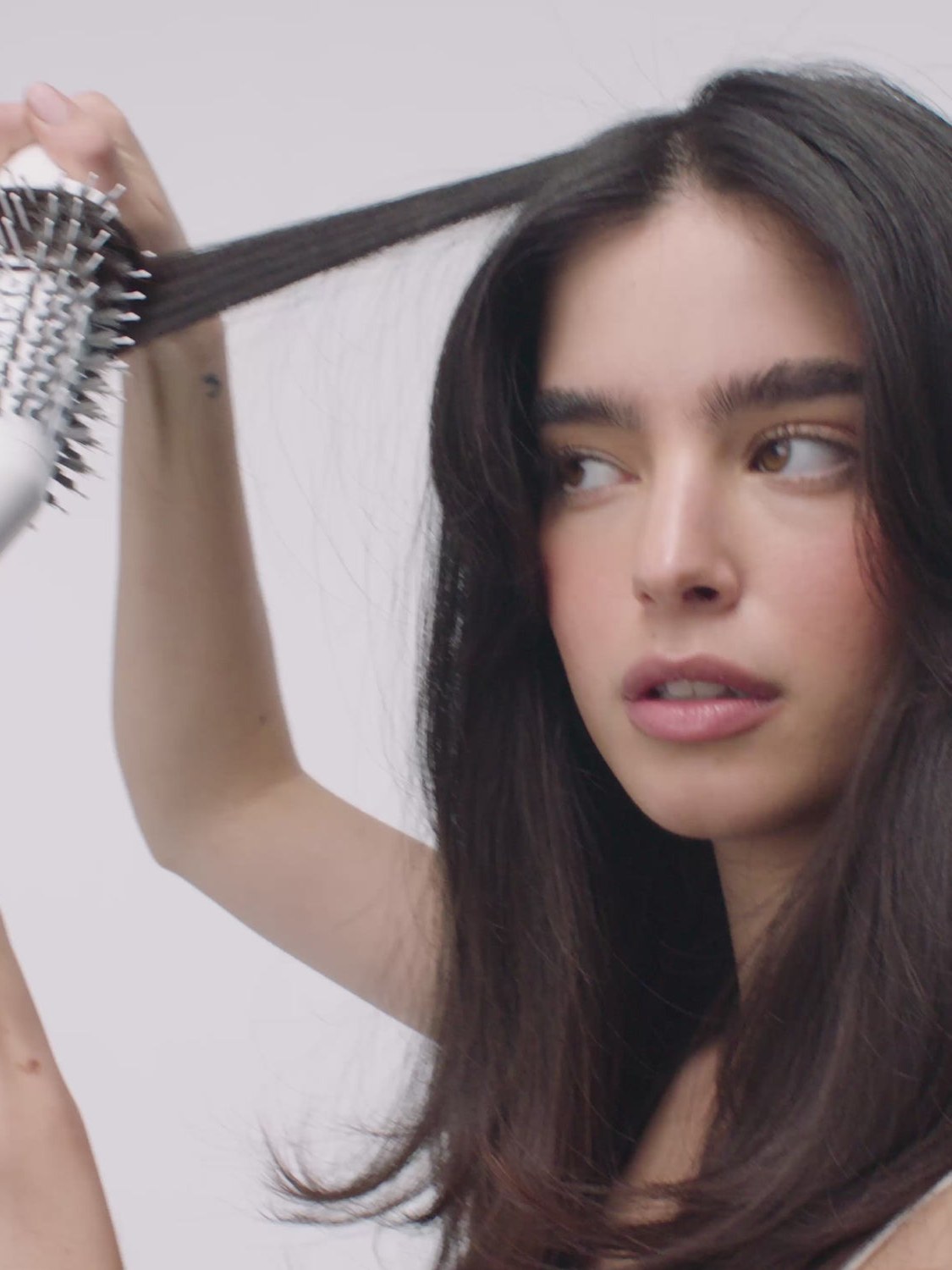 Brunette model brushing a section of hair with a white hot-air brush
