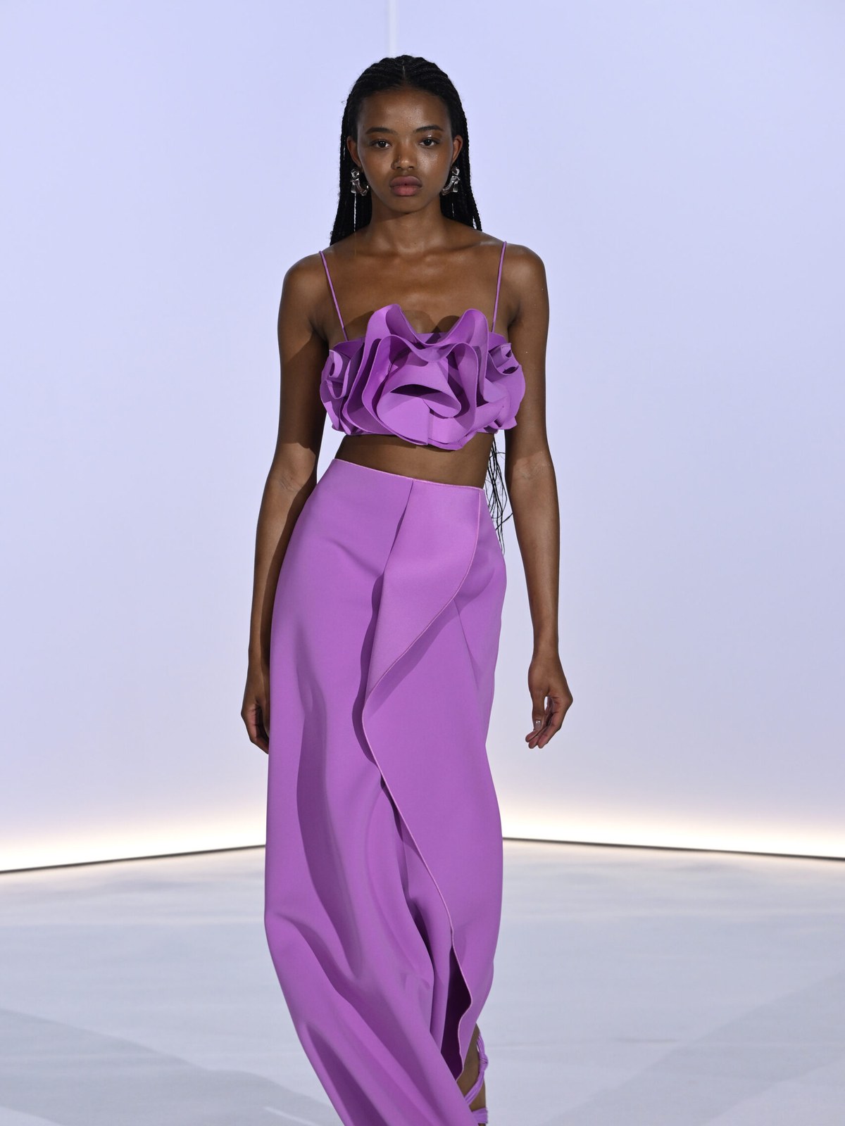 Model in a sculpted purple top and wide-leg trousers on the runway