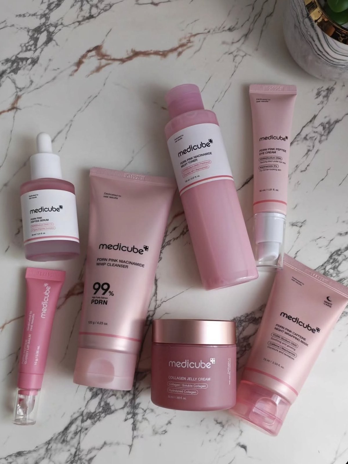 Pink medicube PDRN line of cleanser, toner, serum and masks on a marble counter
