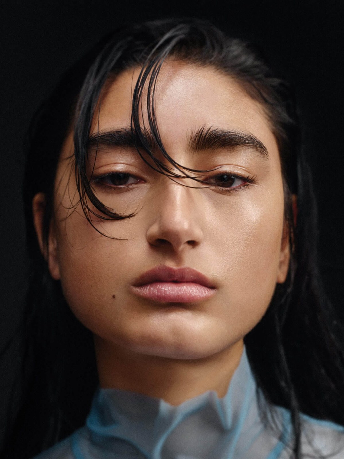 Dark-haired model in a blue blouse against a deep charcoal studio backdrop
