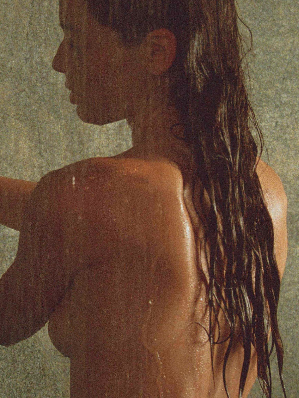 Woman reaching toward Corpus shampoo bottles beside a shower, shown in profile