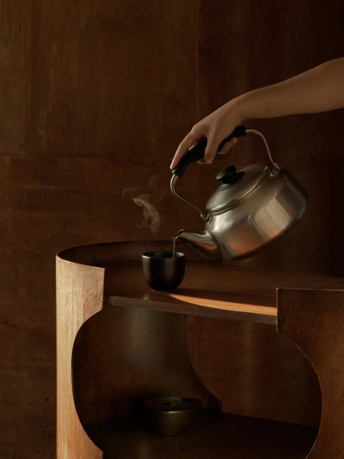 A hand pours hot water beside a quiet wooden table in an Aesop campaign
