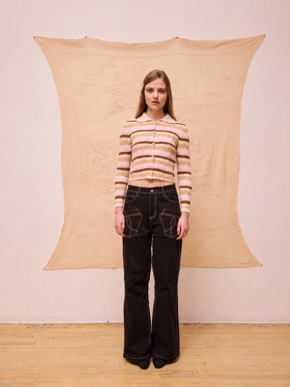 Model in a pink striped cardigan and dark trousers on a textured studio set