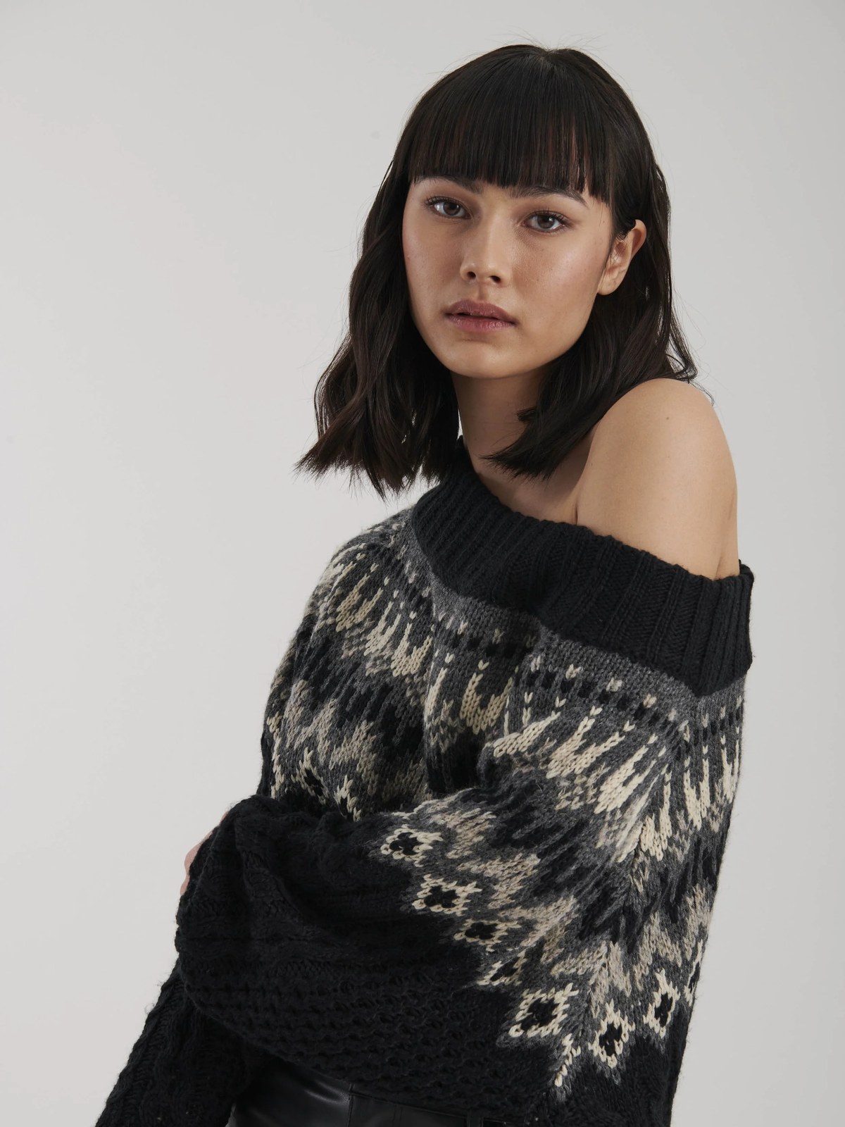 Model wearing a dark patterned off-the-shoulder sweater in a soft studio setting
