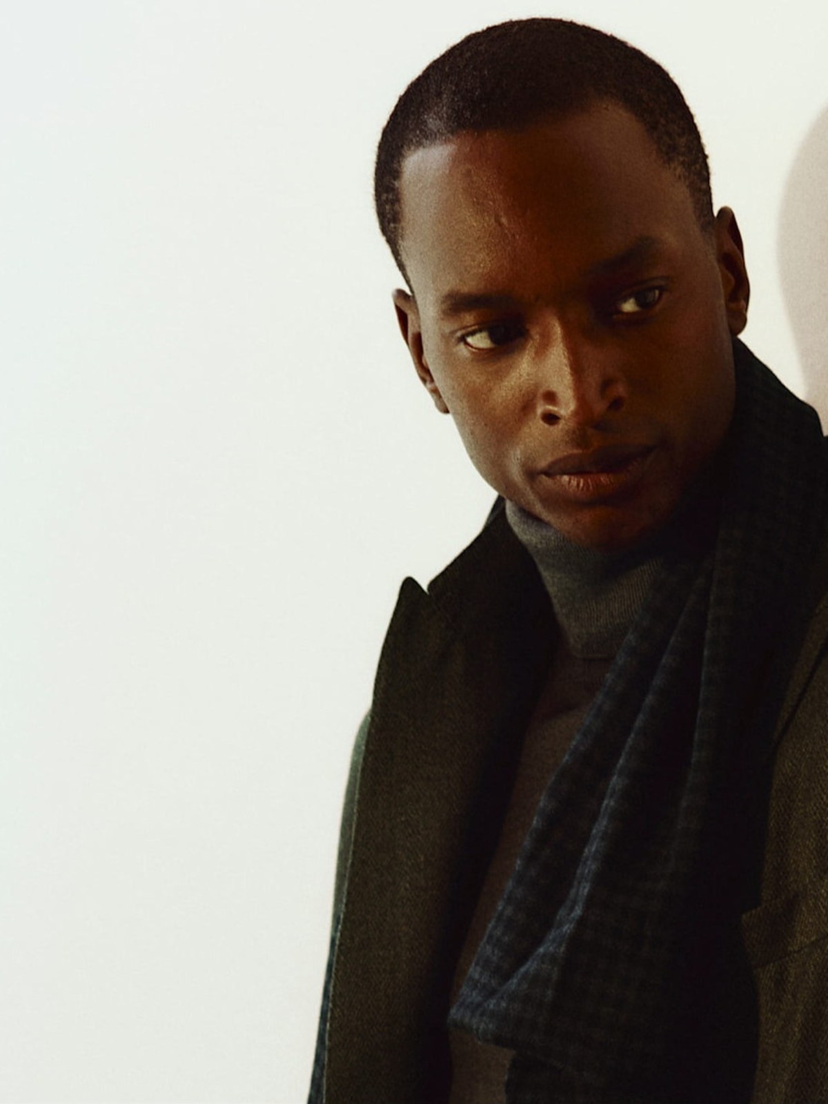 Two men in layered fall outerwear and a scarf against a pale wall