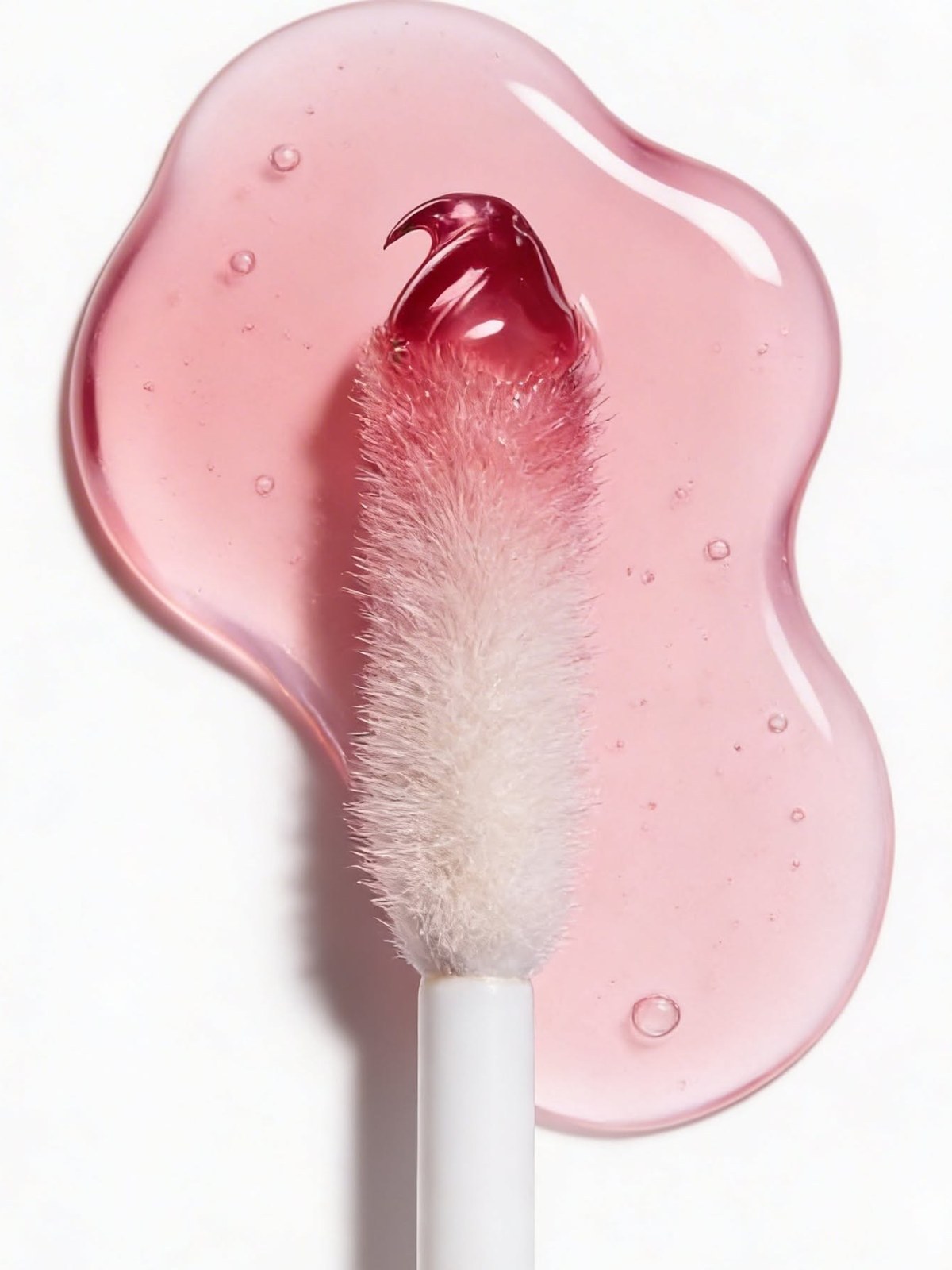Pink lip oil swatch with a fluffy white applicator resting in the clear pool of product
