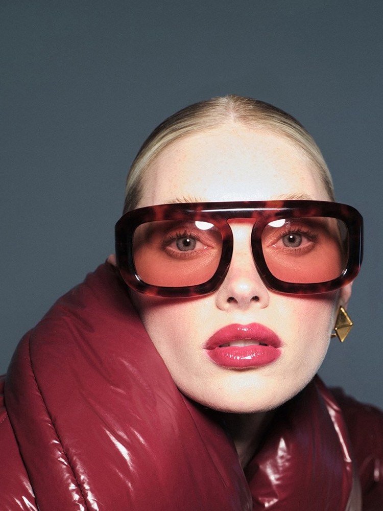 Elsa Hosk in burgundy quilted outerwear and red glasses in a campaign portrait