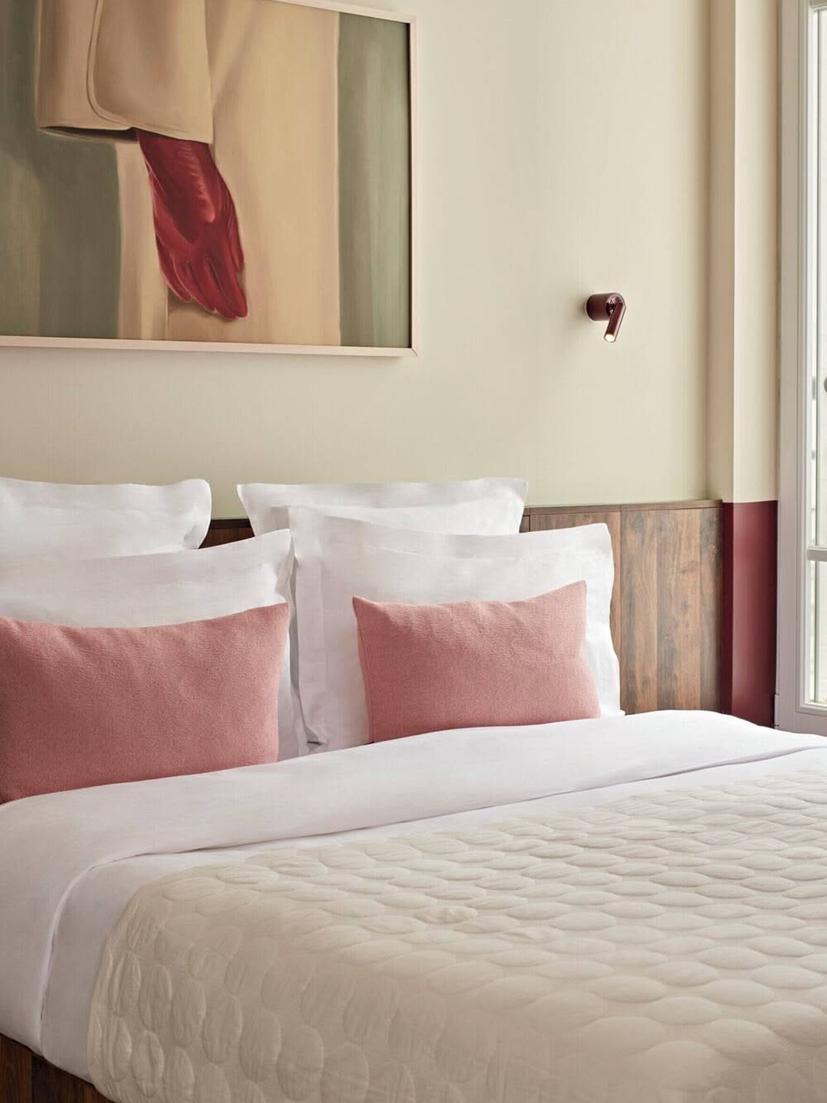 Bed with white linen, two pink cushions and a painting of a red glove above a wood headboard