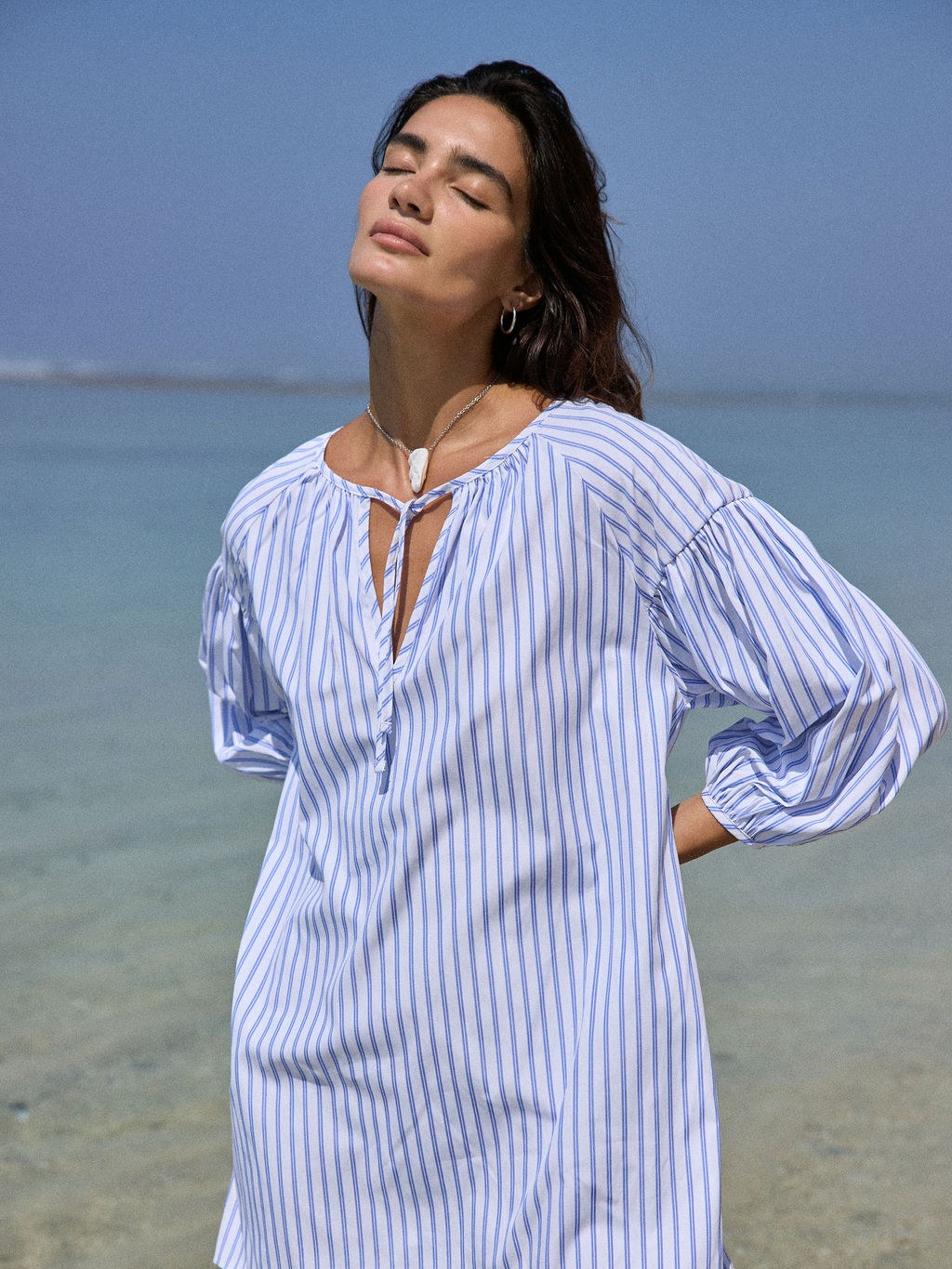 Model in a blue striped dress standing at the water's edge