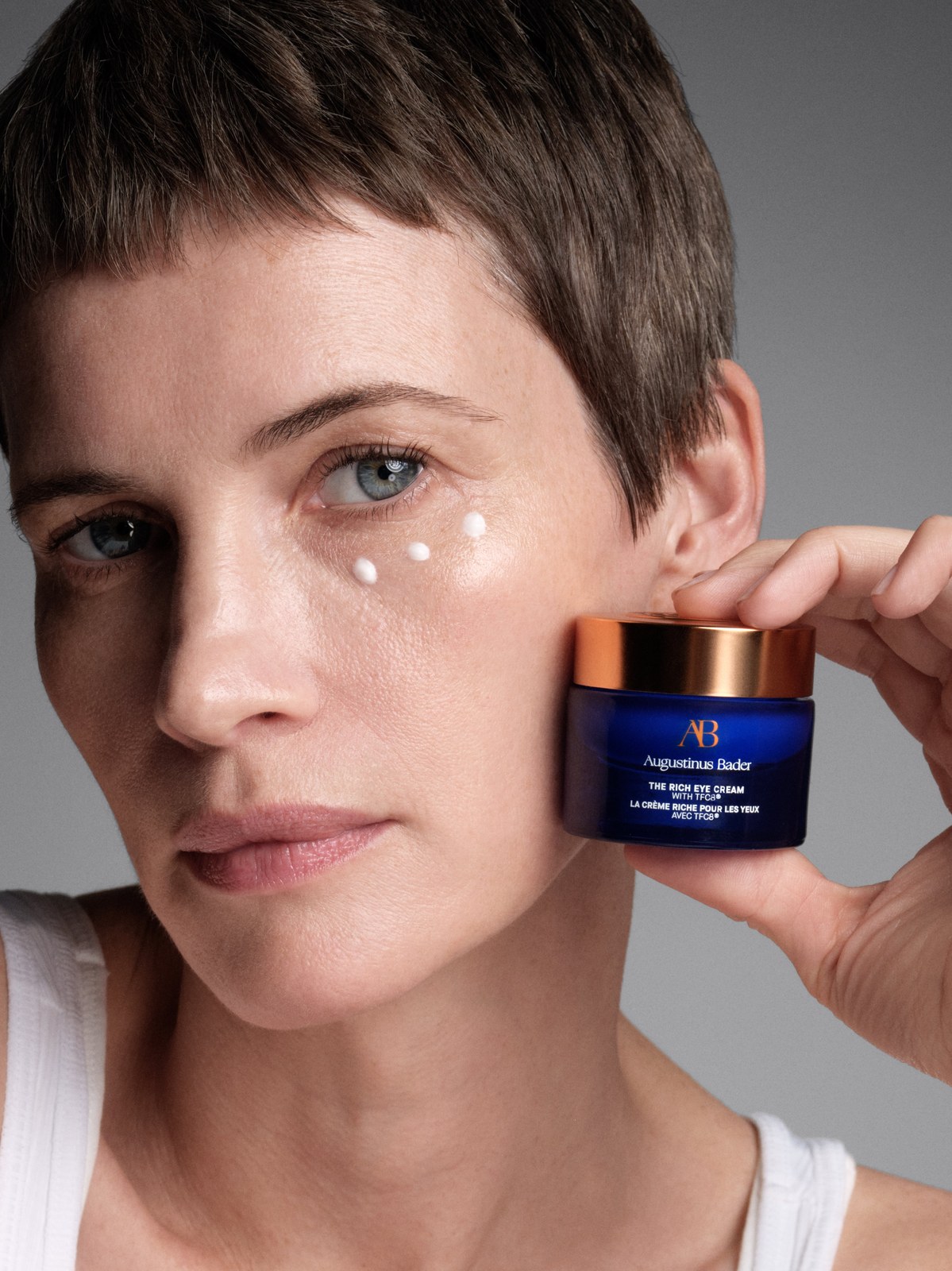 Short-haired woman holding a jar of eye cream beside her face