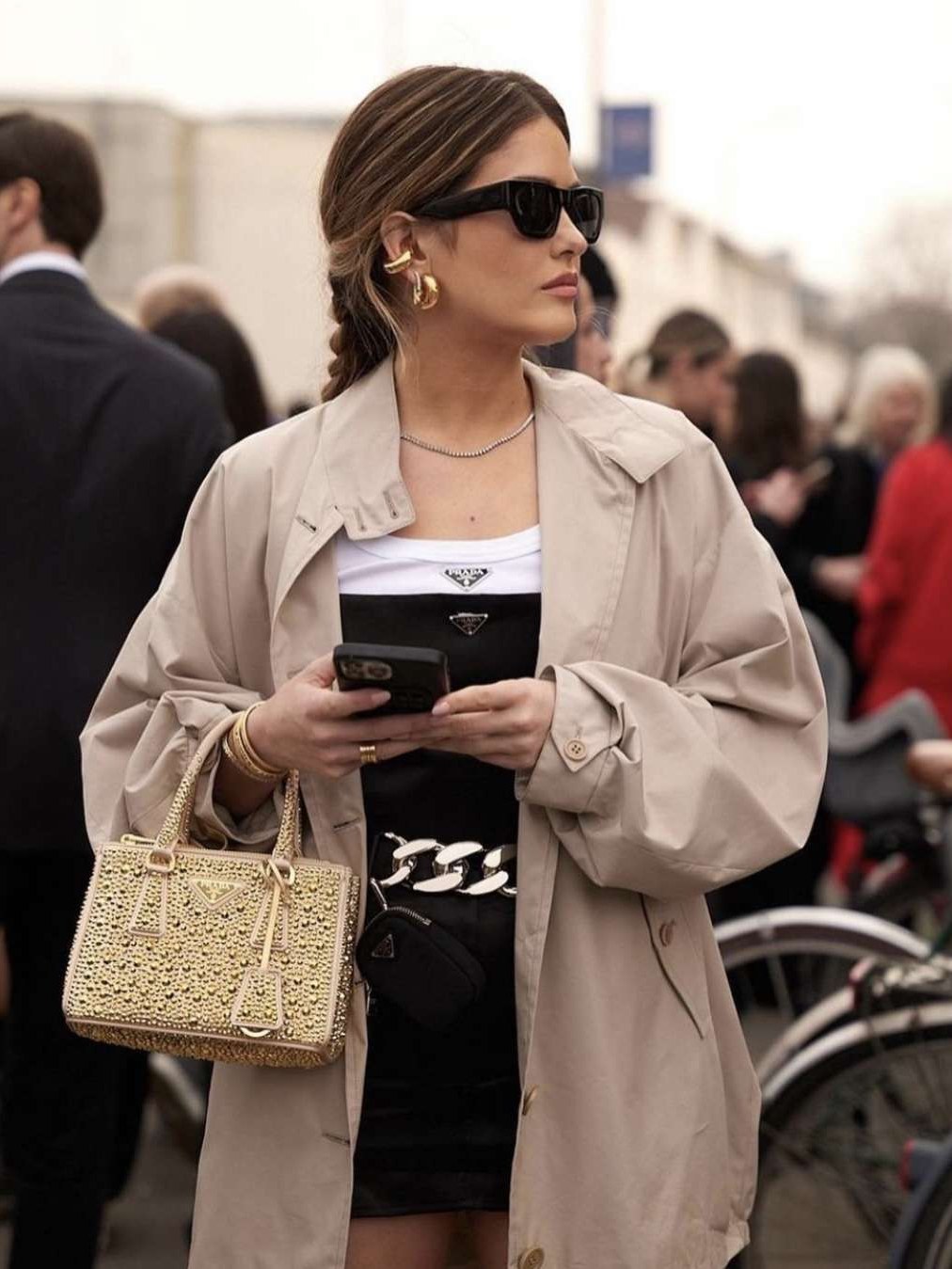 Woman in a pale coat and sunglasses carrying a structured light-colored handbag on a city street