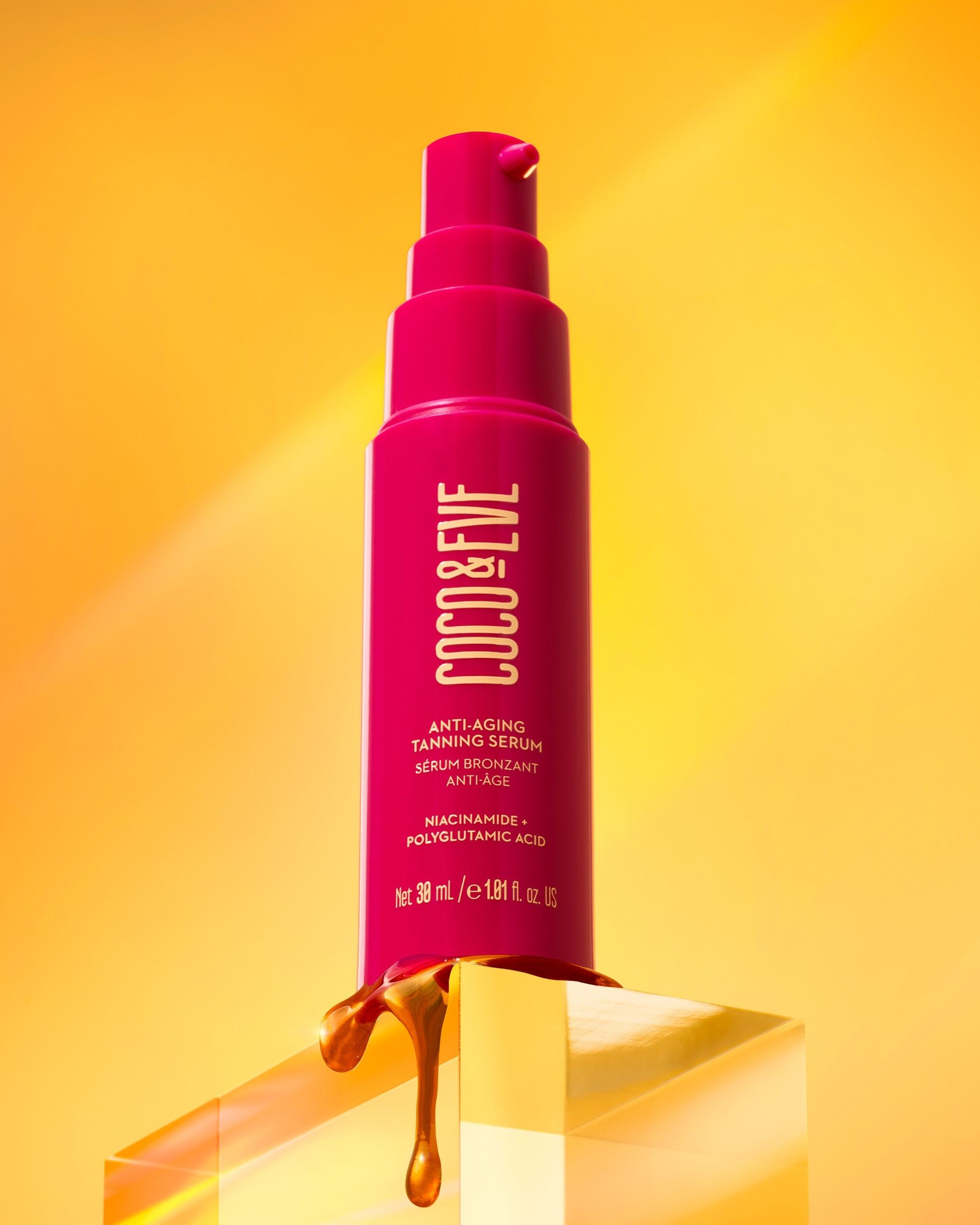 Magenta Coco & Eve Anti-Aging Tanning Serum bottle on a glass block with honey-colored drips against a golden yellow background