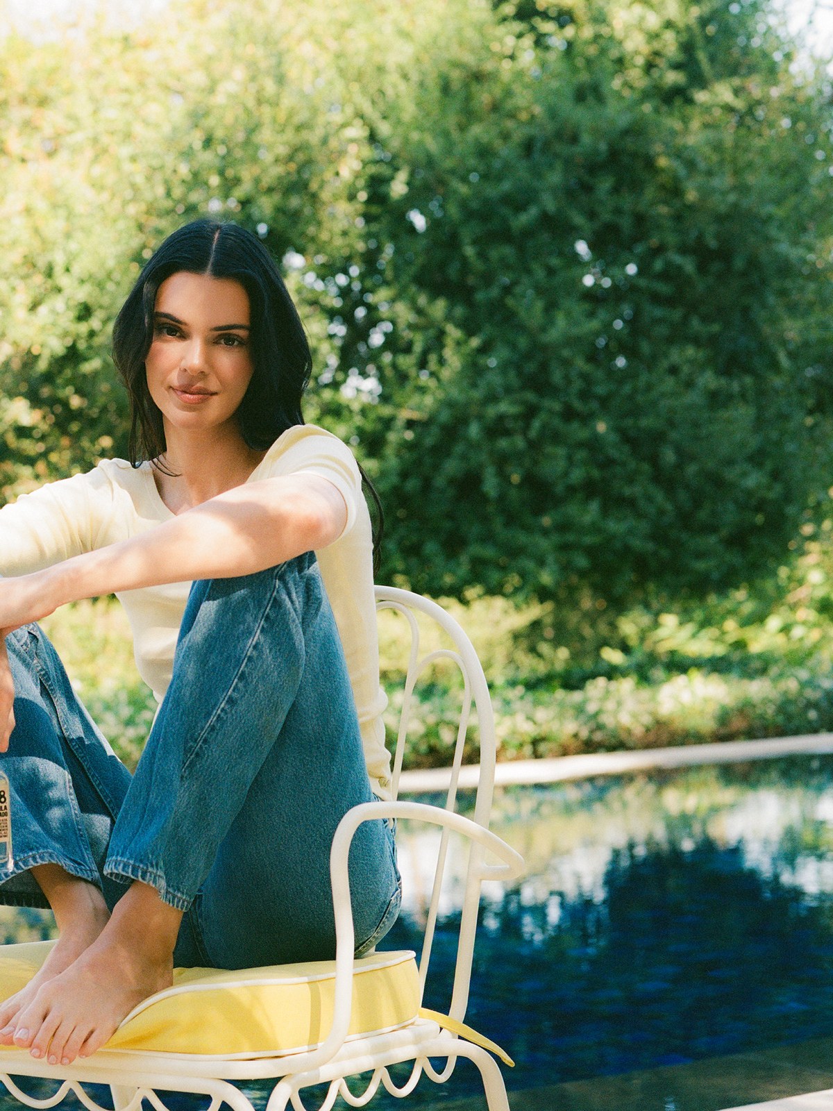 Woman seated on a yellow cushioned white metal chair beside a garden pool