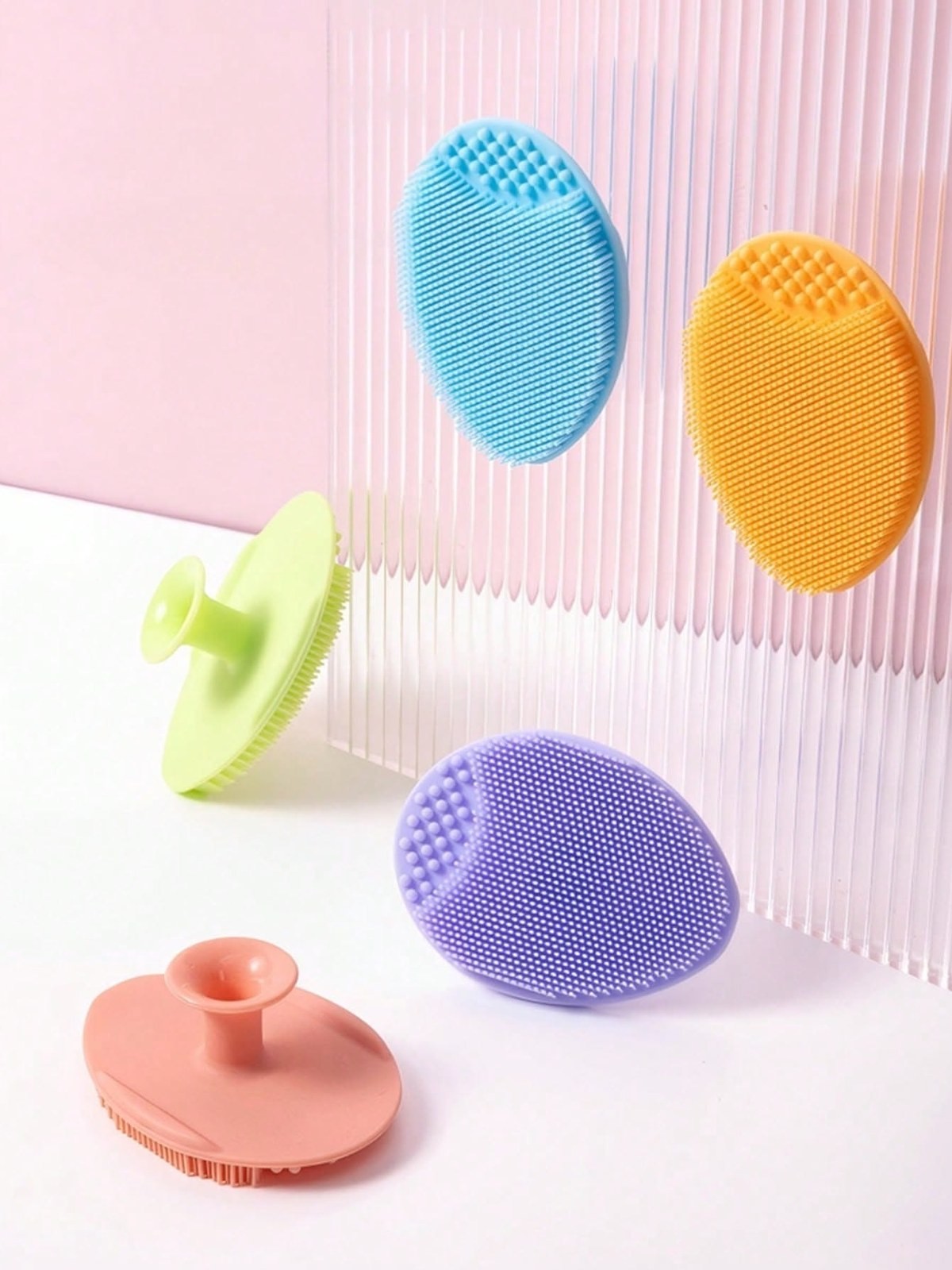 Colorful silicone facial cleansing scrubbers in blue, orange, green, purple and pink arranged against a pink background