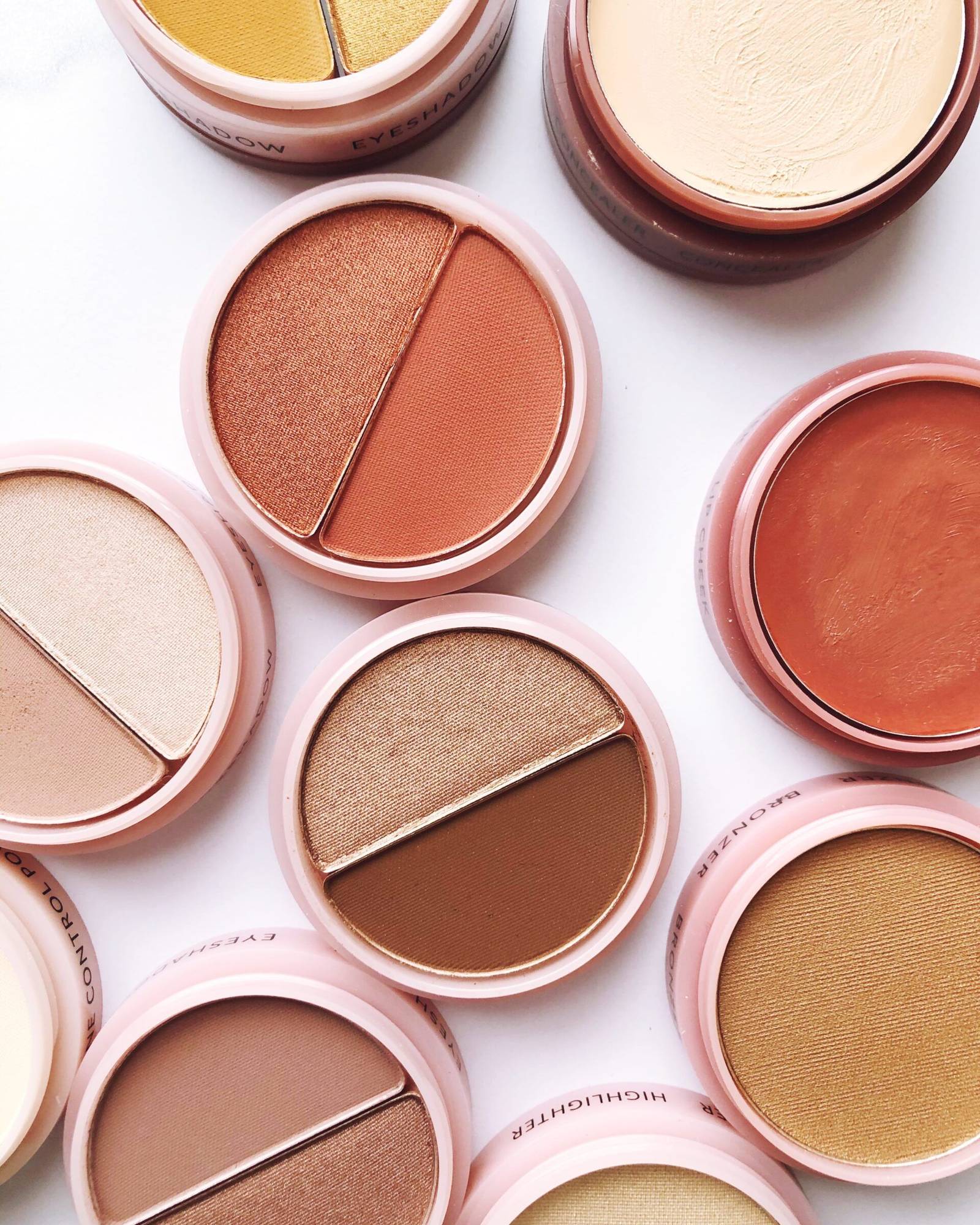 Overhead view of round pink makeup compacts in terracotta, bronze and peach shades with cream concealer and cream blush
