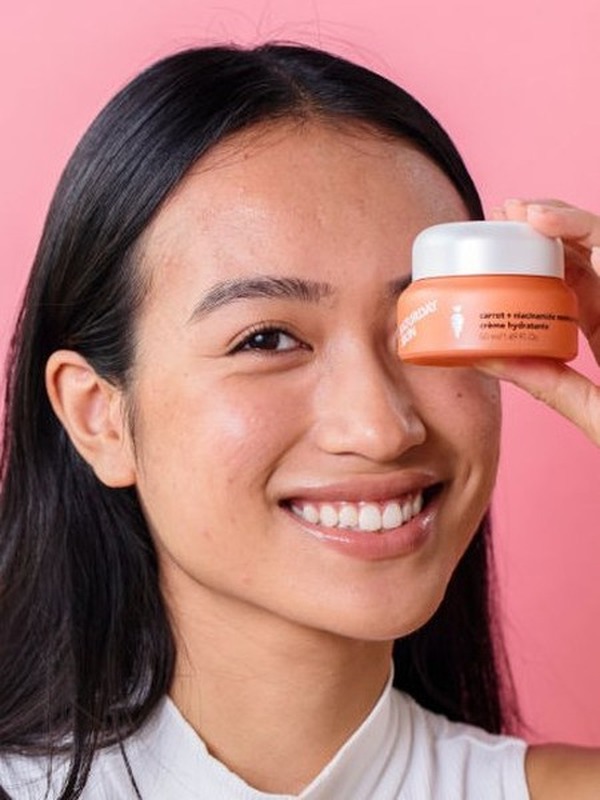 Woman holding a Saturday Skin carrot cream jar near her face