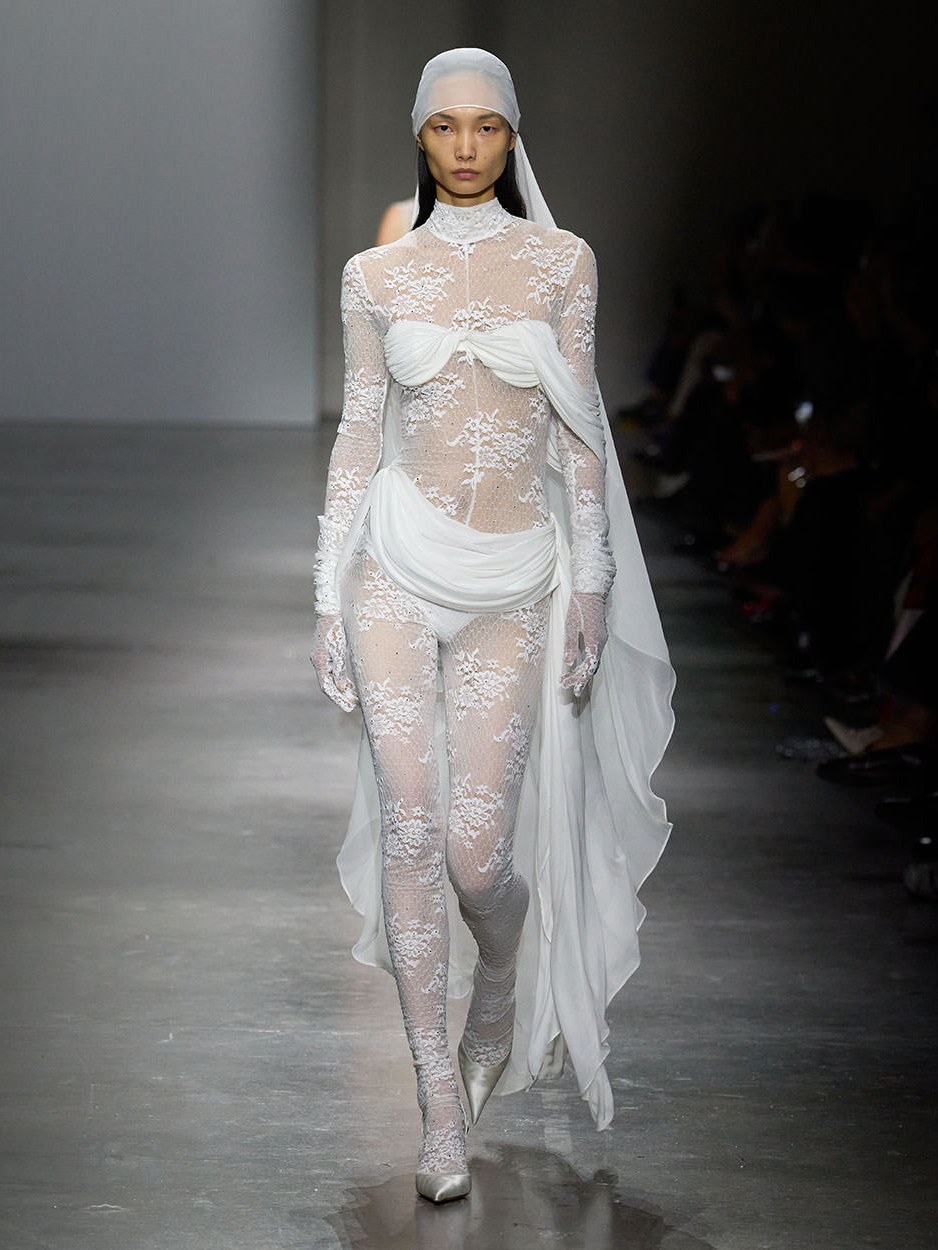 Model in a sheer white lace look walking the Spring Summer 2026 runway