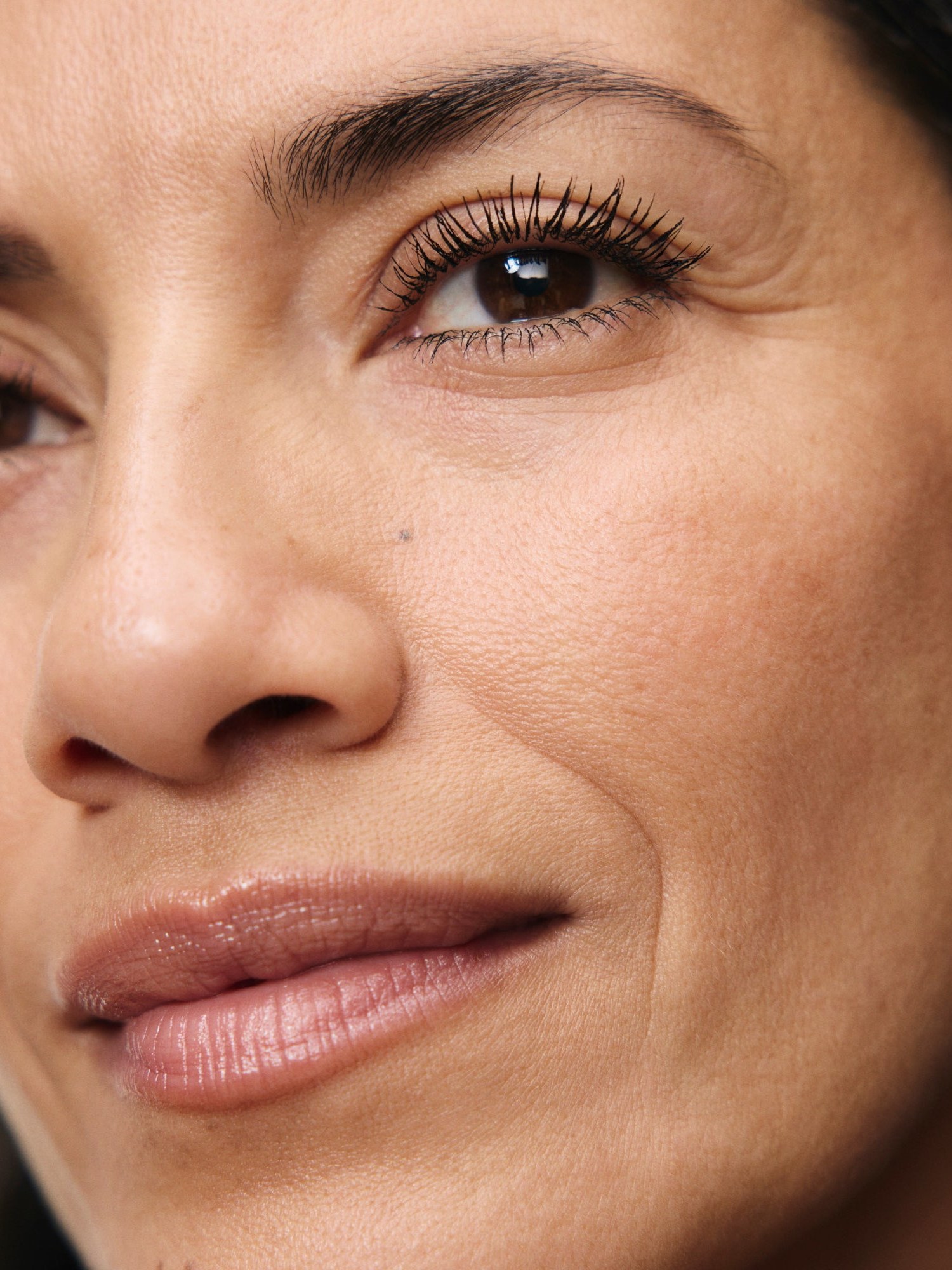 Tight crop of a woman's eye with defined lashes and a nude lip