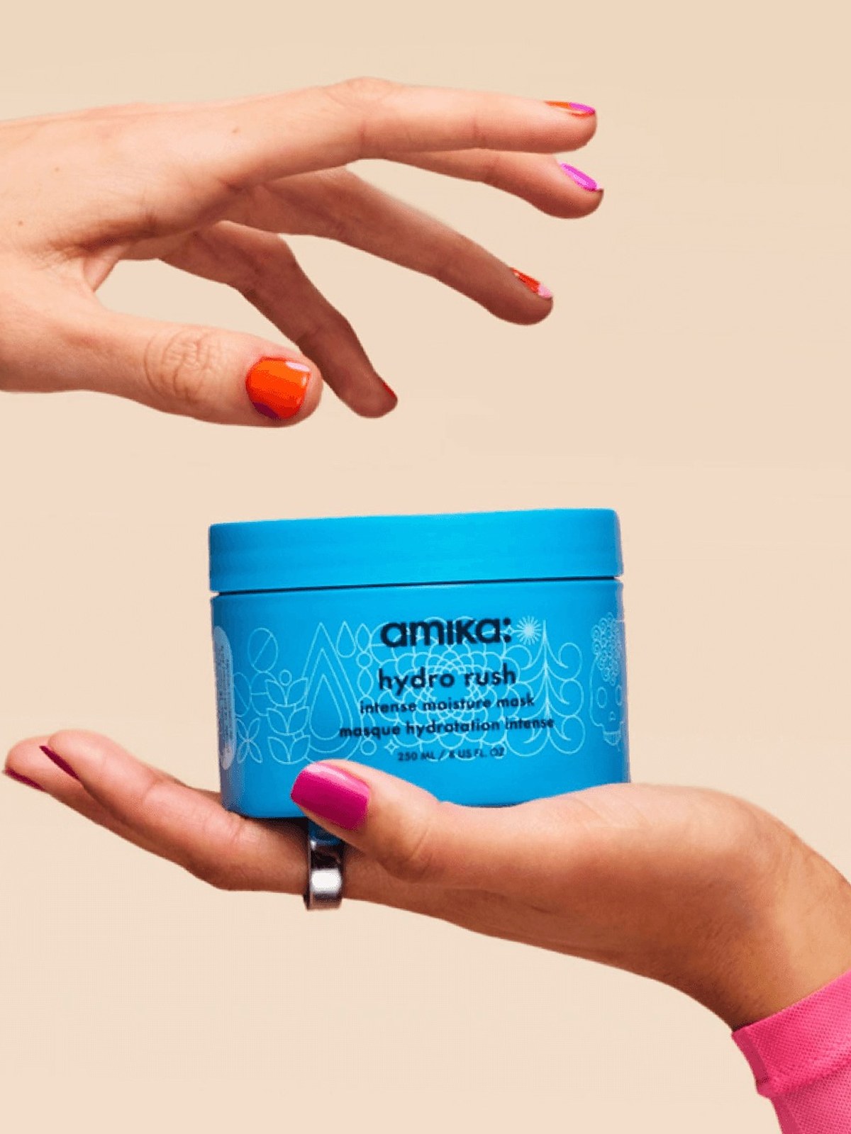 Hand holding an amika hydro rush mask jar against a beige backdrop