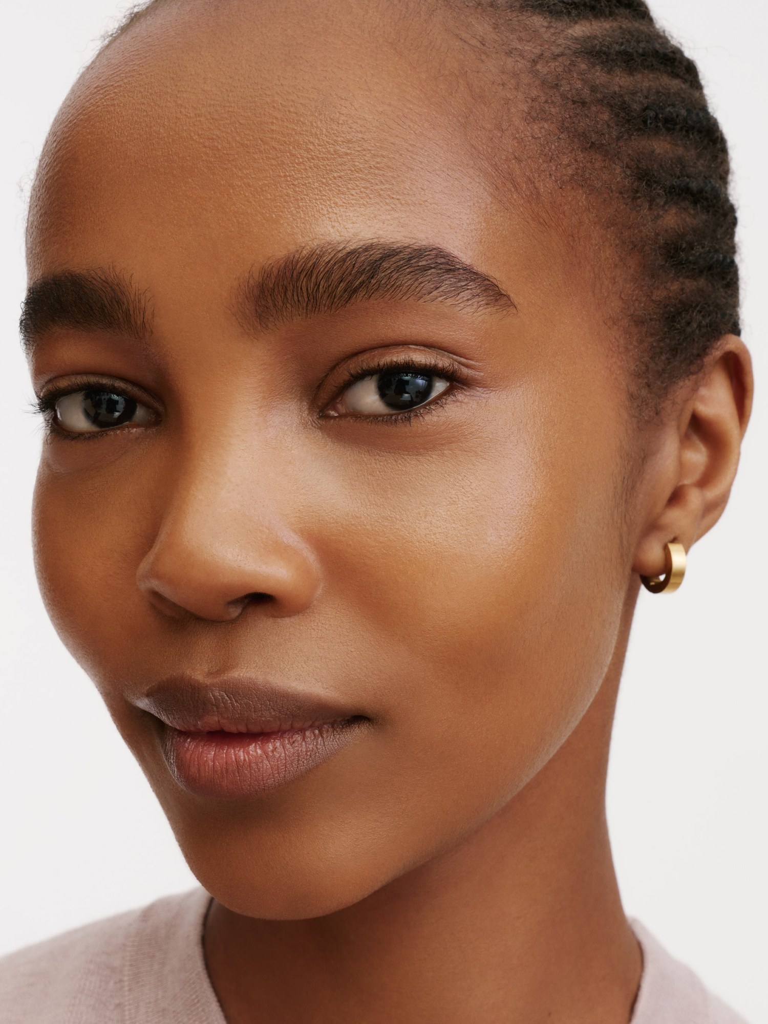 Close portrait of a model with a soft nude lip and gold hoop earring