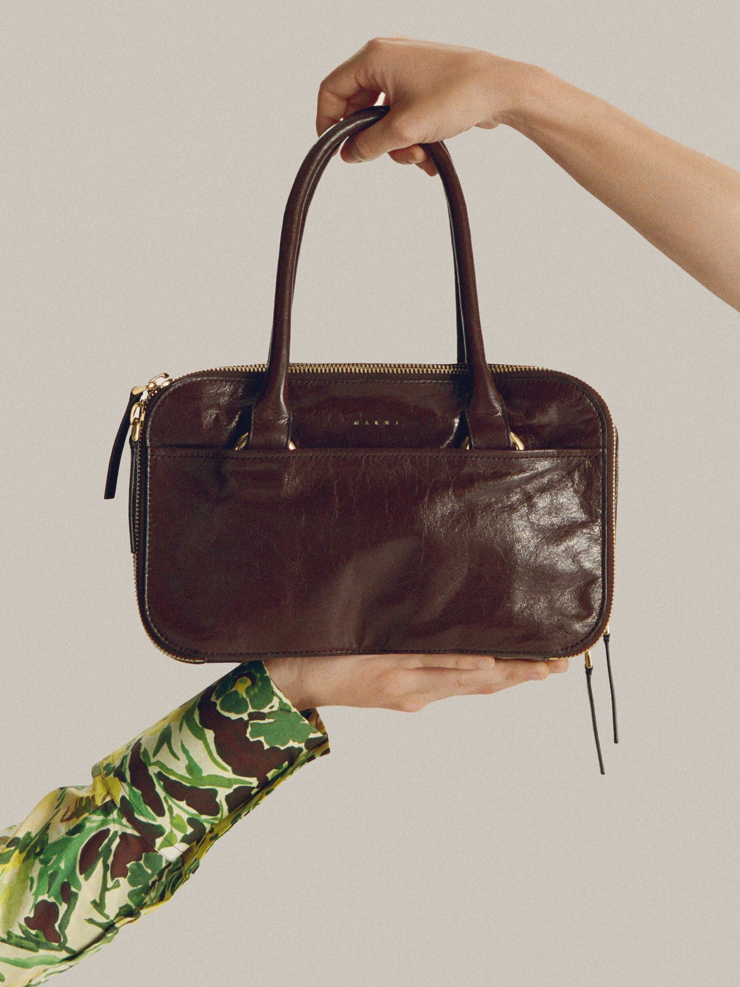 Hand holding a glossy brown leather top handle bag