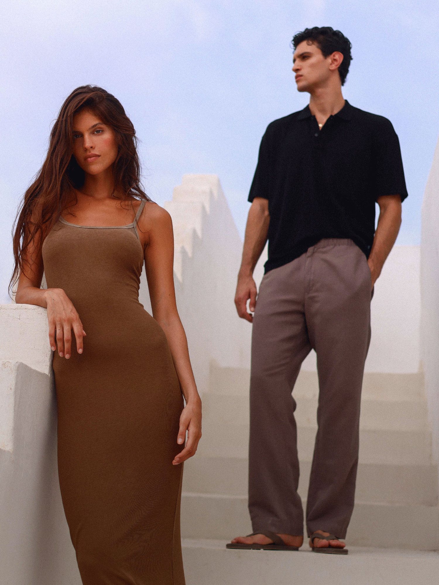 Woman in a brown dress and man in a black polo on white stucco stairs