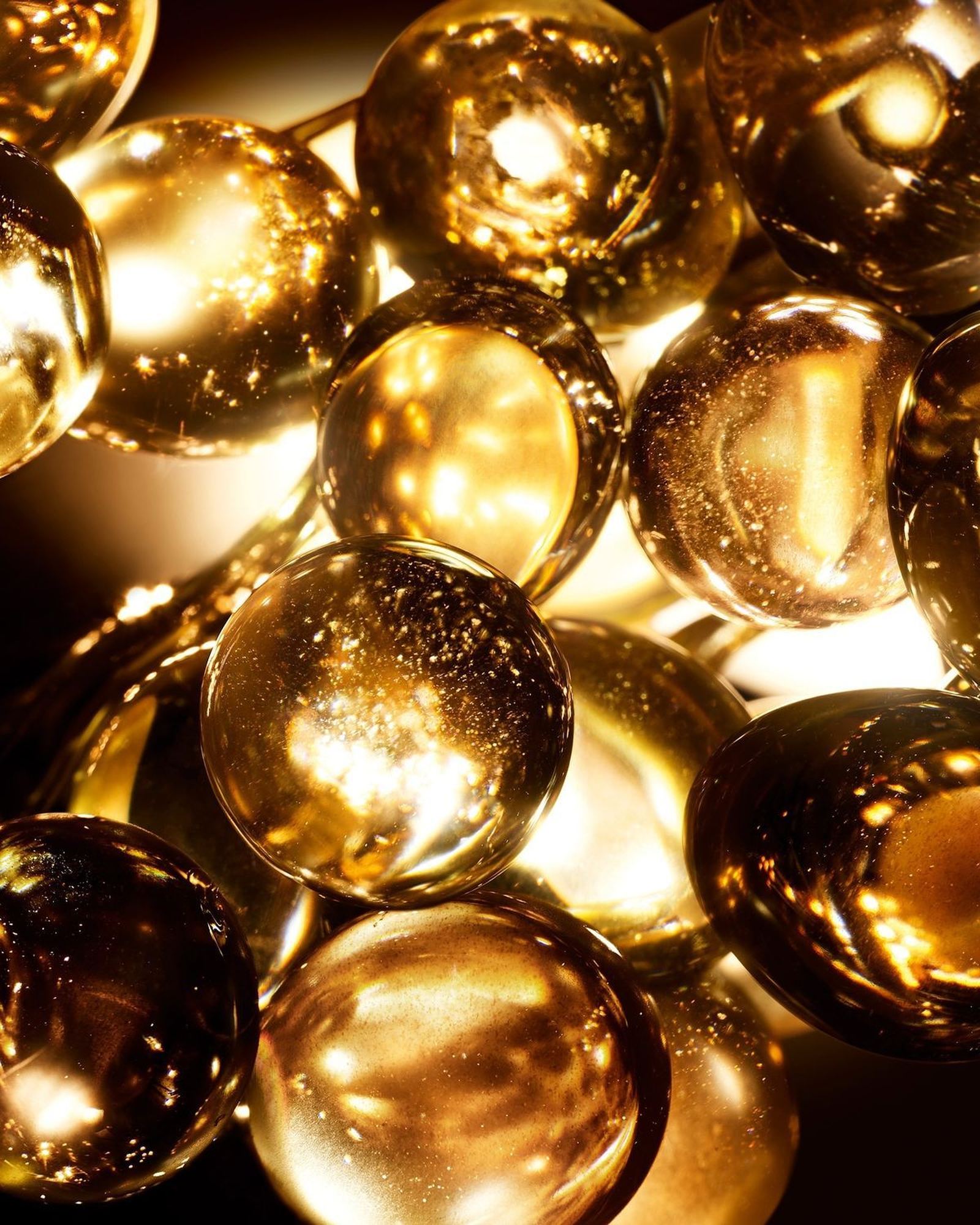 Close-up of glossy golden droplets lit from behind, like oil beads or capsules, on a dark background