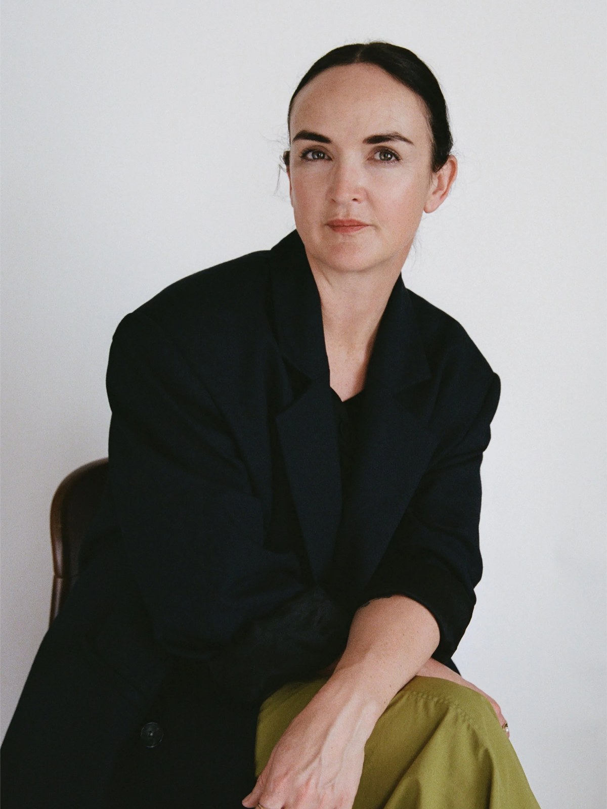 Founder Frances Shoemack seated in a black jacket and olive trousers.