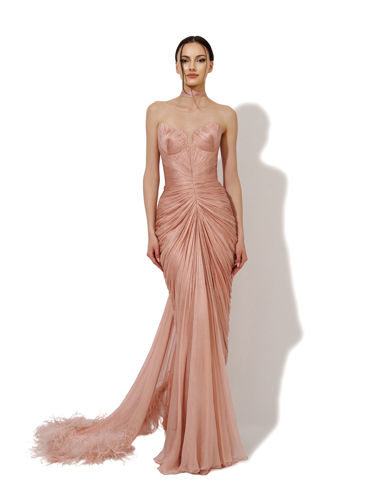 Model in a blush pink ruched gown with a feathered train