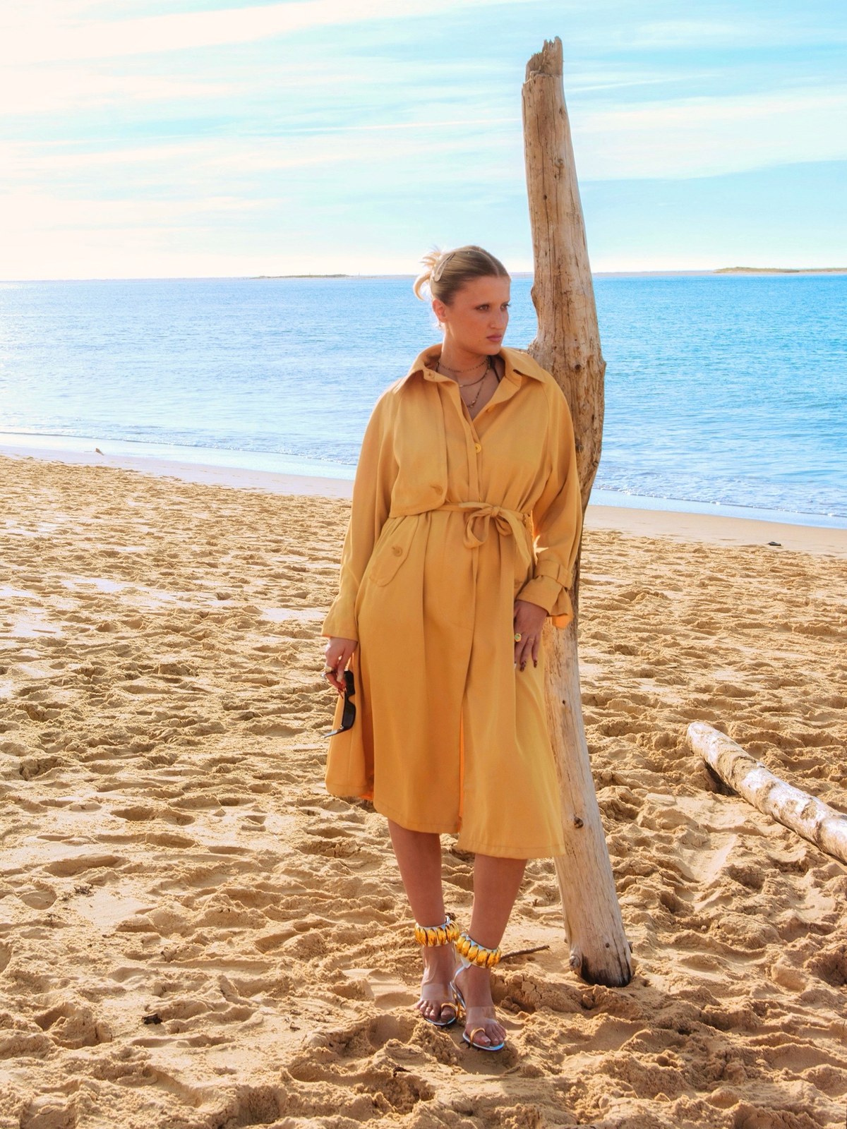 Model in a yellow belted dress and sandals on a beach