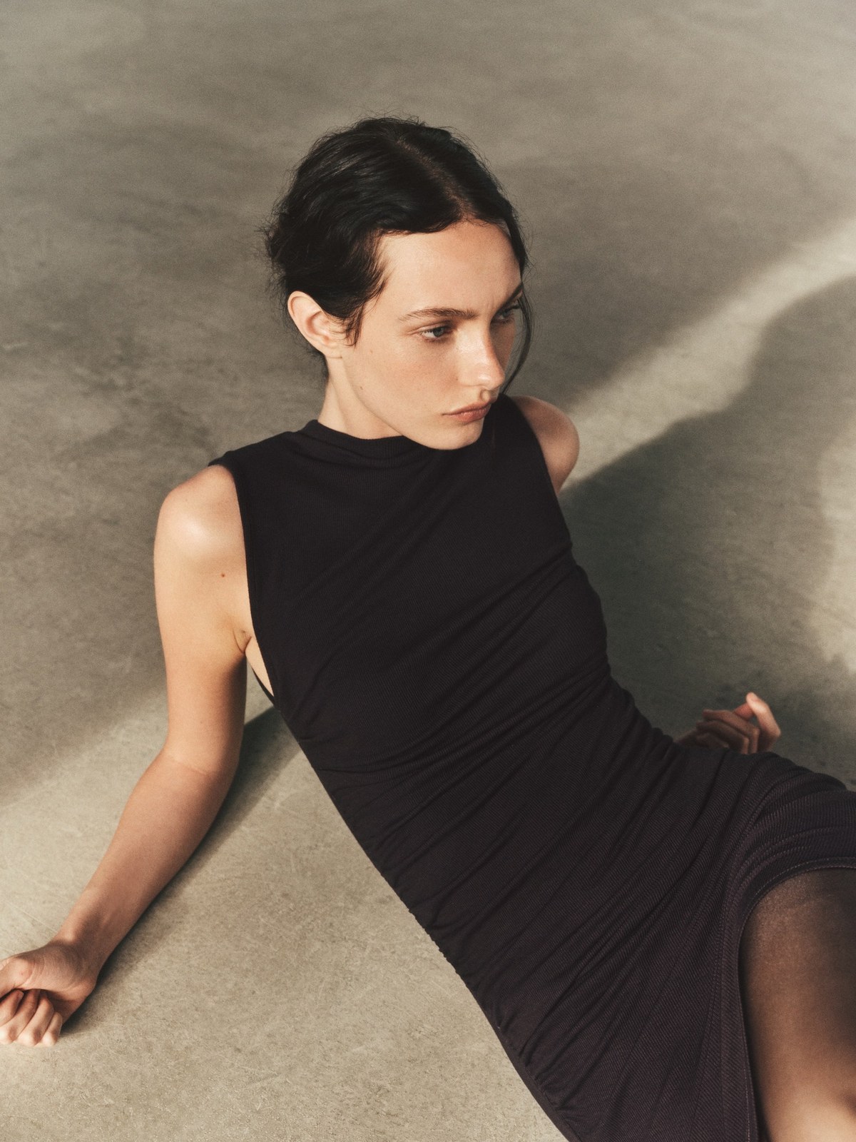Model in a sleeveless black dress reclining on a textured floor