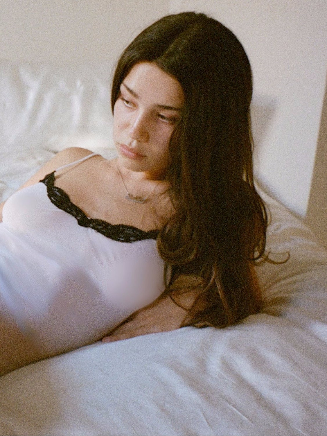 Model in a white lace-trimmed top reclining on a bed