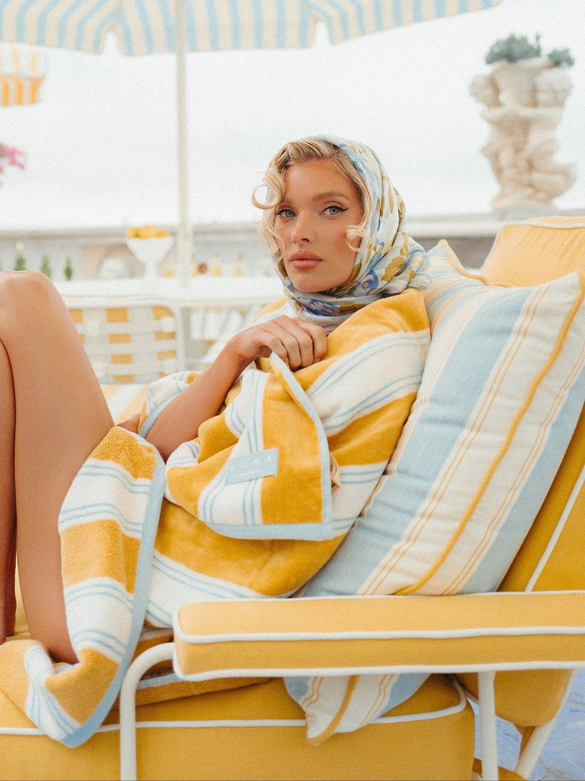 Woman reclining on a yellow and white striped sun lounger with a matching towel at a poolside patio