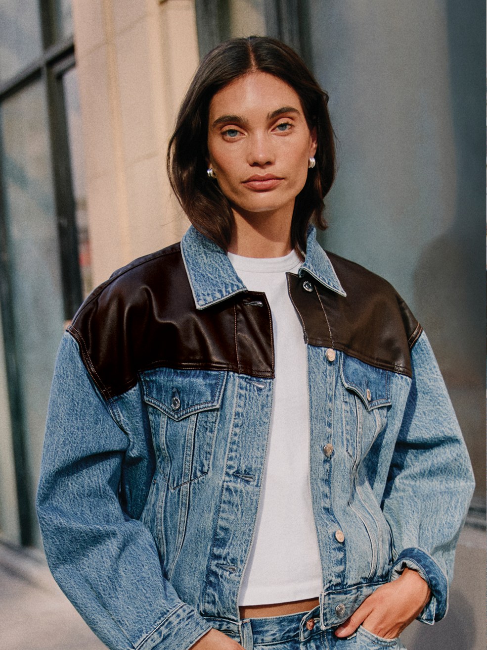 Model in a denim and brown jacket layered over jeans against a city wall