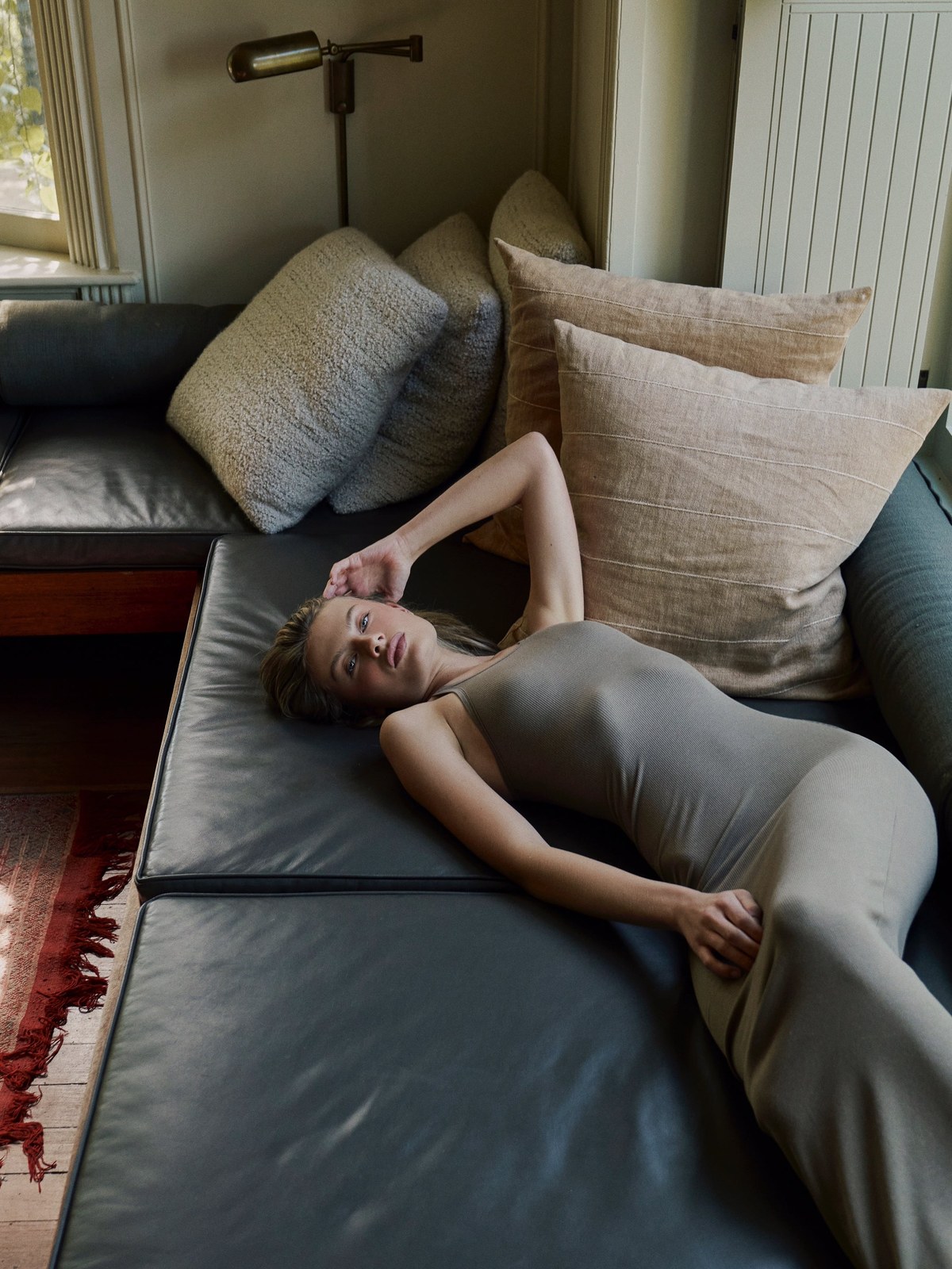 Model in a taupe CLYQUE bodysuit relaxing on a sofa at home