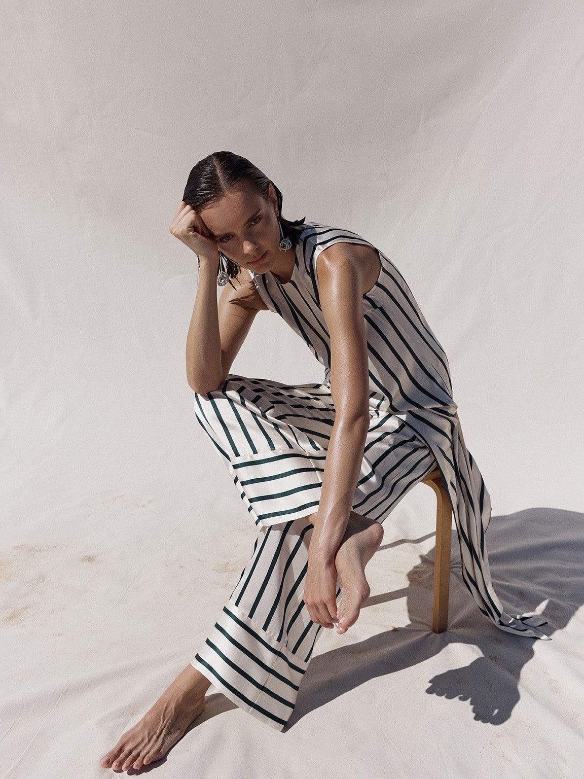 Model in a striped resort outfit seated in bright studio light