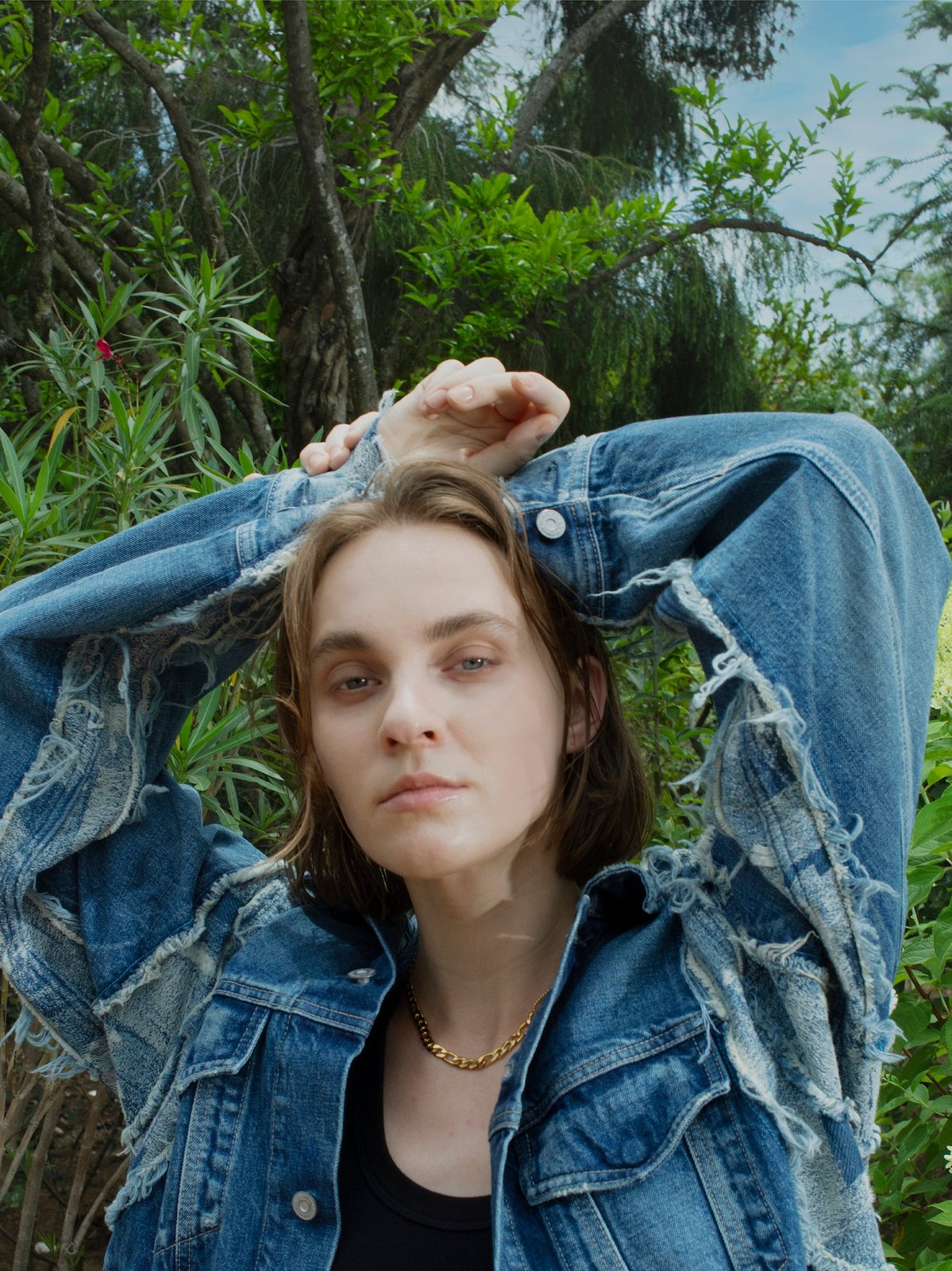 Model in a distressed denim jacket in a leafy garden