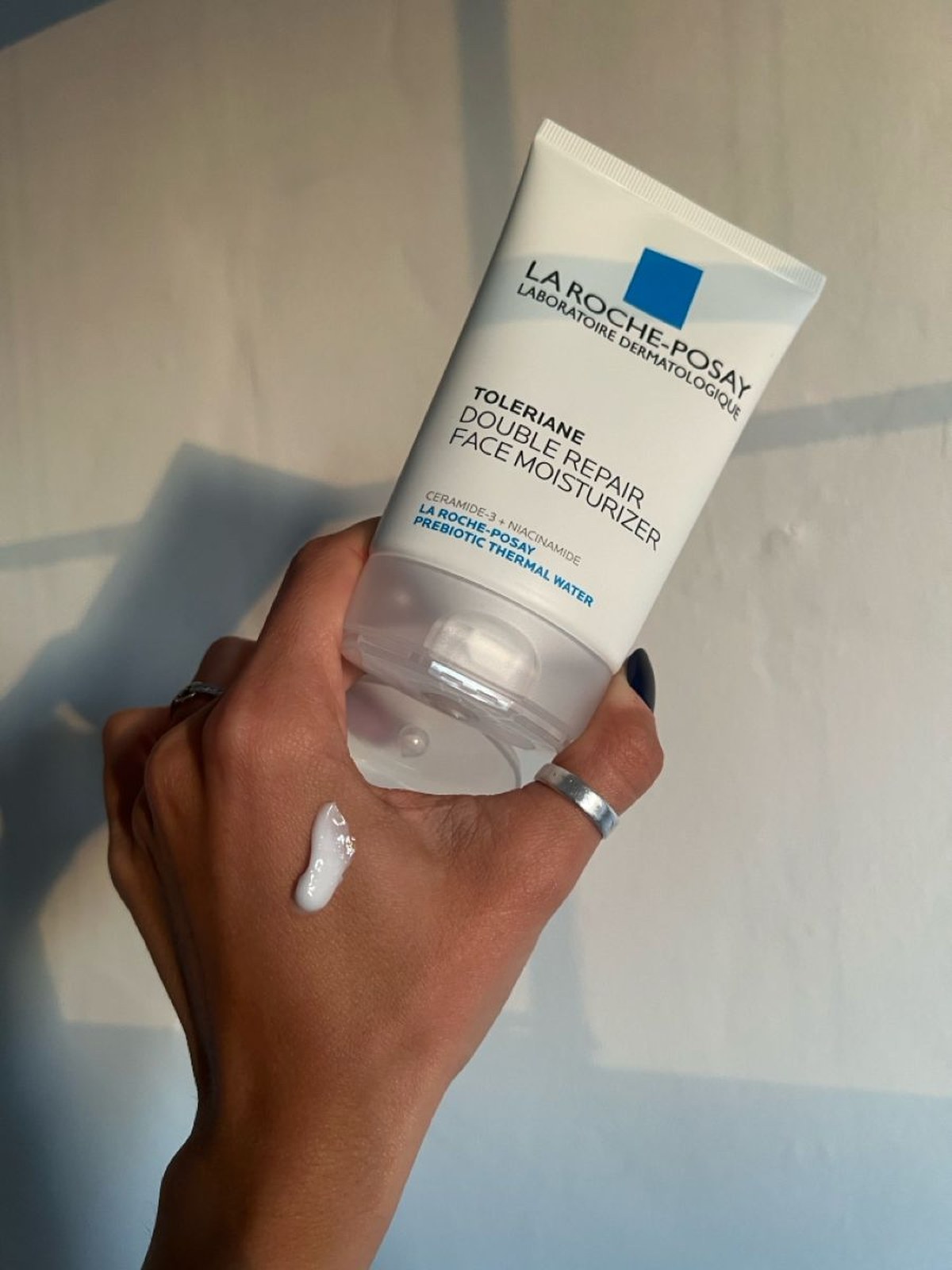 Hand holding a tube of La Roche-Posay Toleriane Double Repair Face Moisturizer with a white swatch of cream on the back of the hand