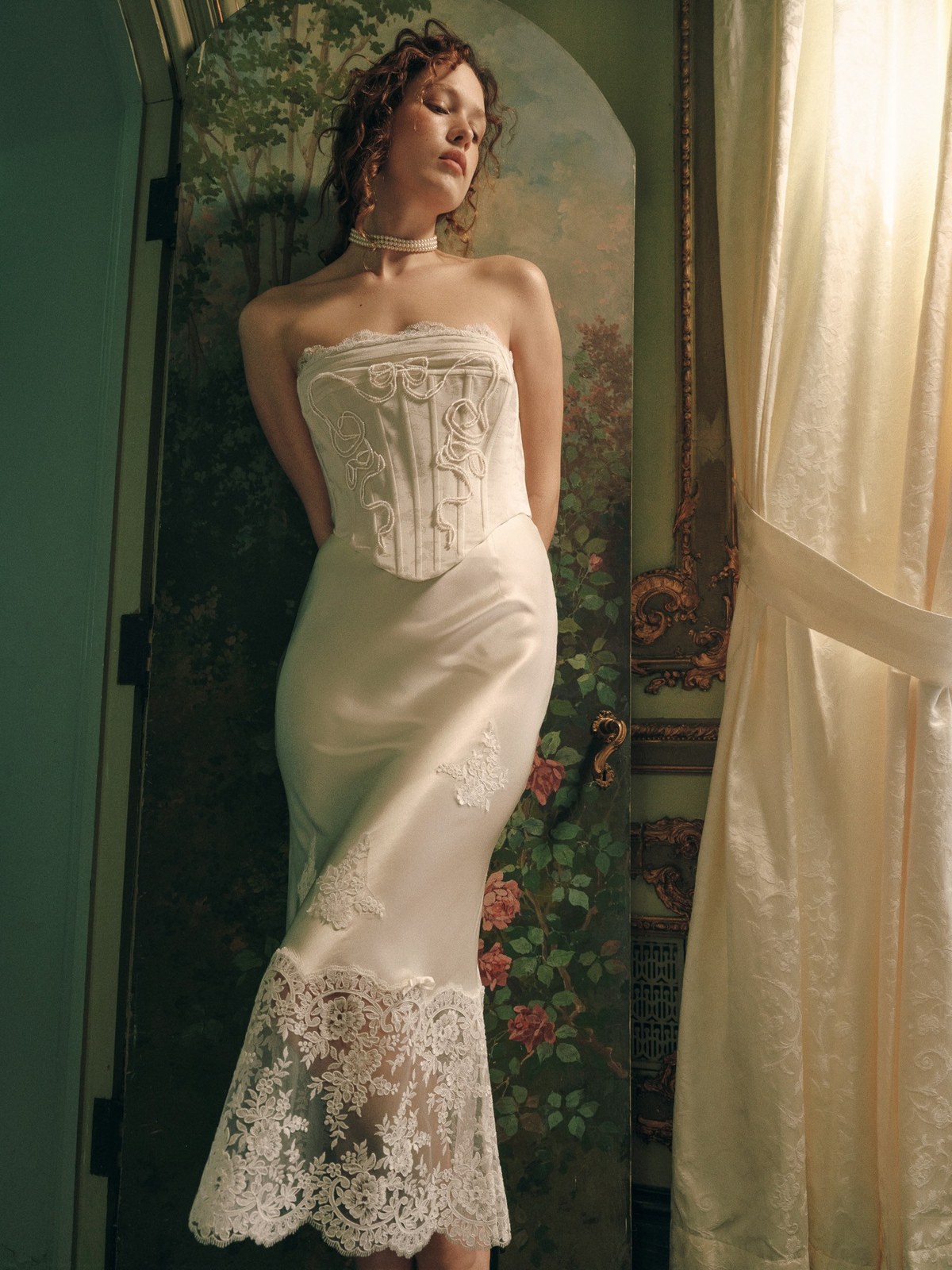 Model in an ivory corset and lace dress beside a painted floral doorway