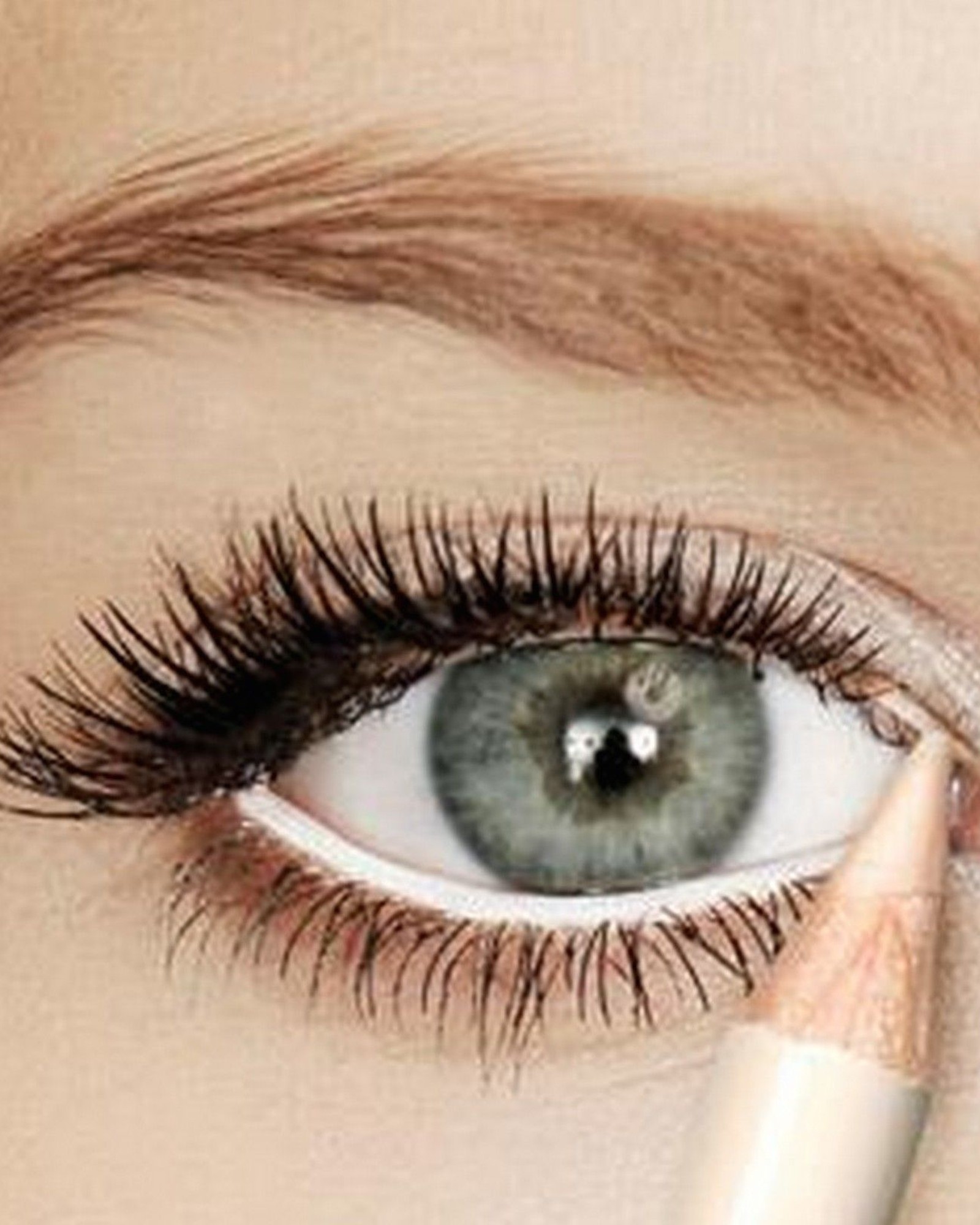 Extreme close-up of a grey eye with long lashes while a white pencil lines the waterline