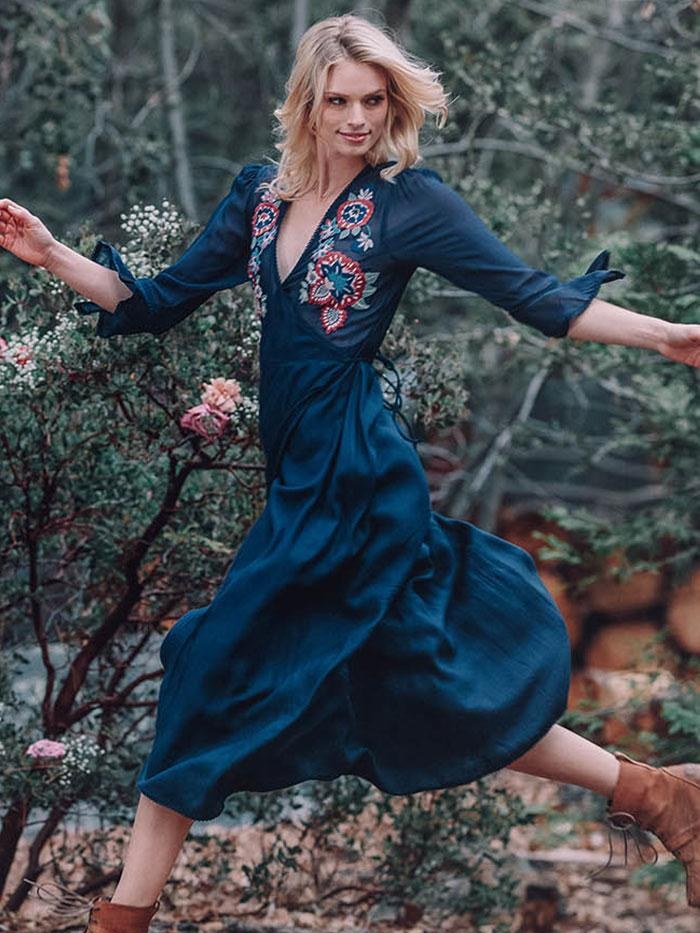 Woman in a blue embroidered dress moving through a garden