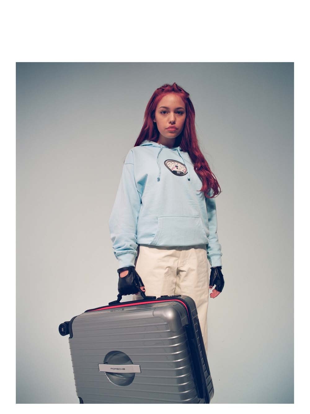 Woman in a pale sweatshirt standing beside a silver suitcase